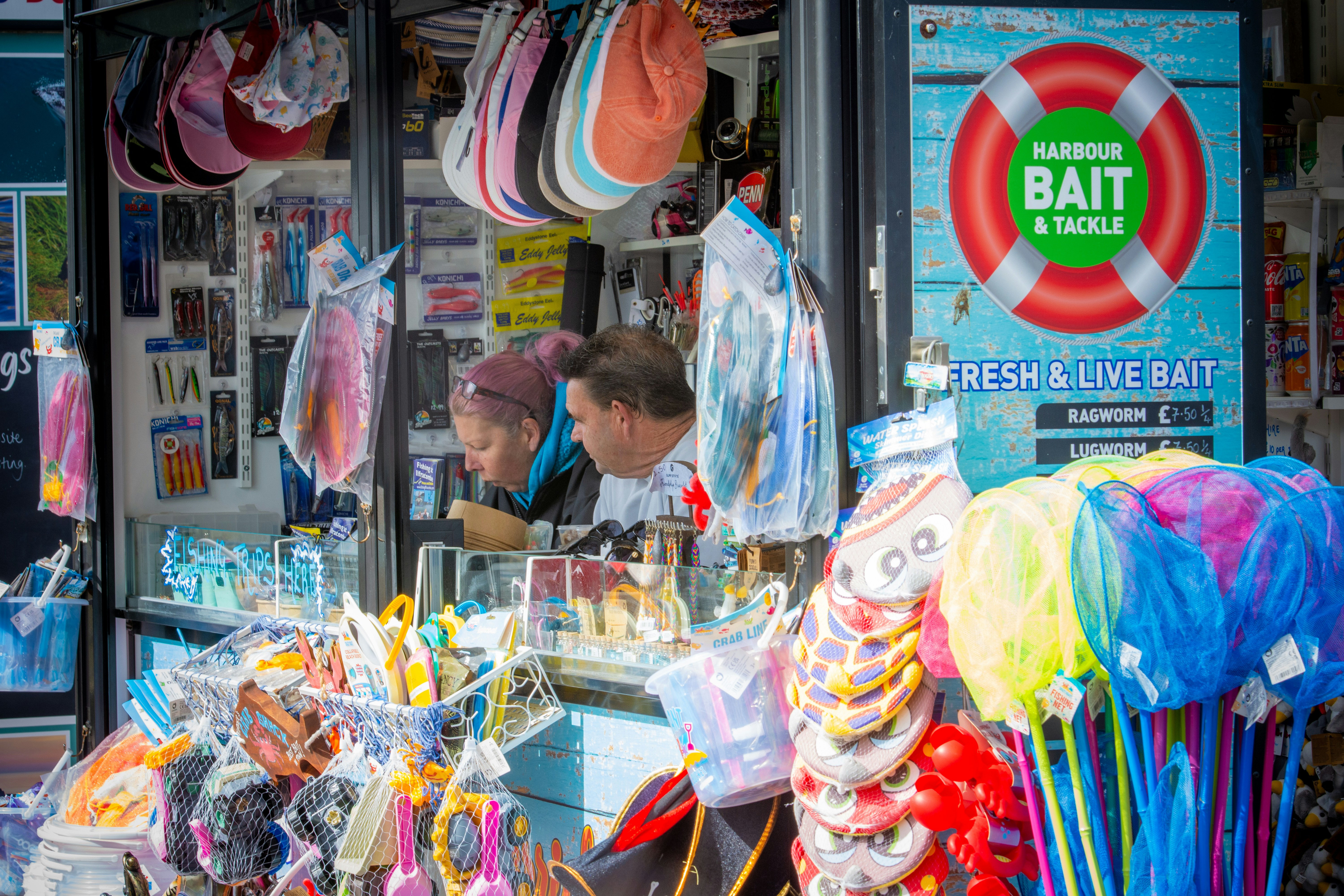 People looking at bait and tackle at a seaside shop.
