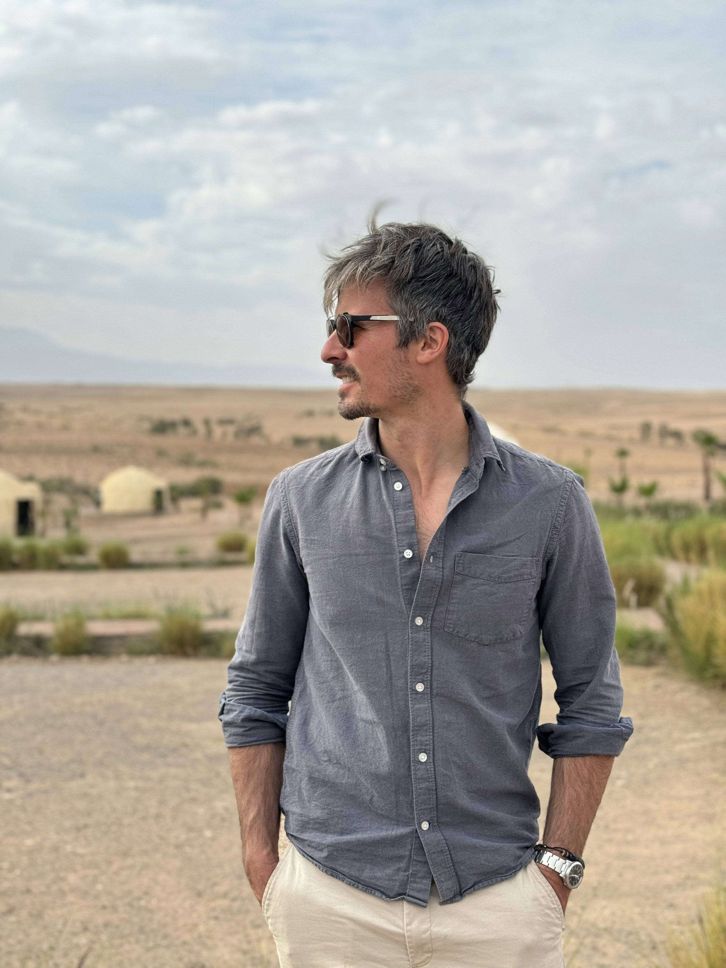 Man in sunglasses and button-up shirt in desert landscape.