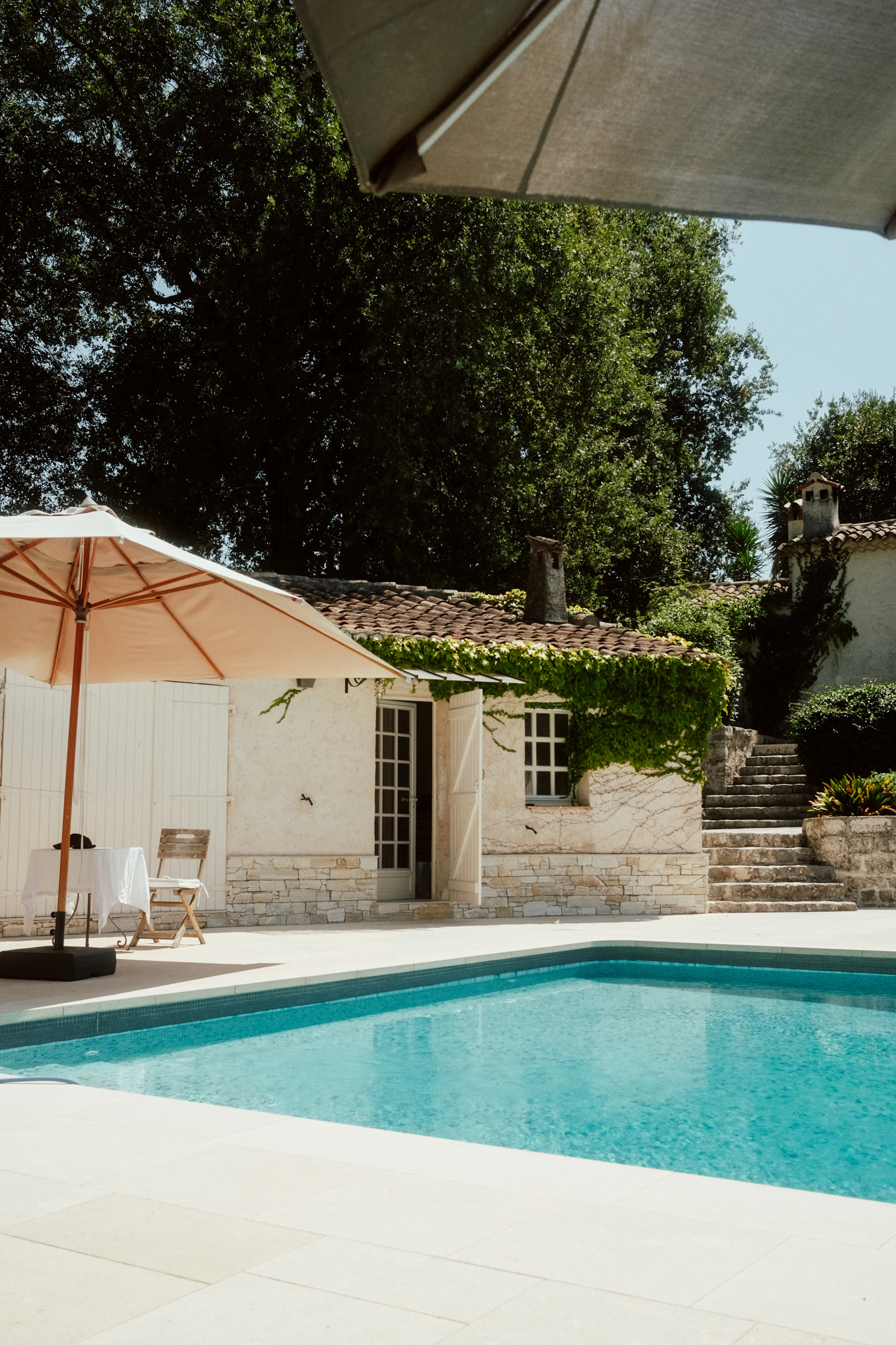 A swimming pool and patio with umbrellas and chairs.