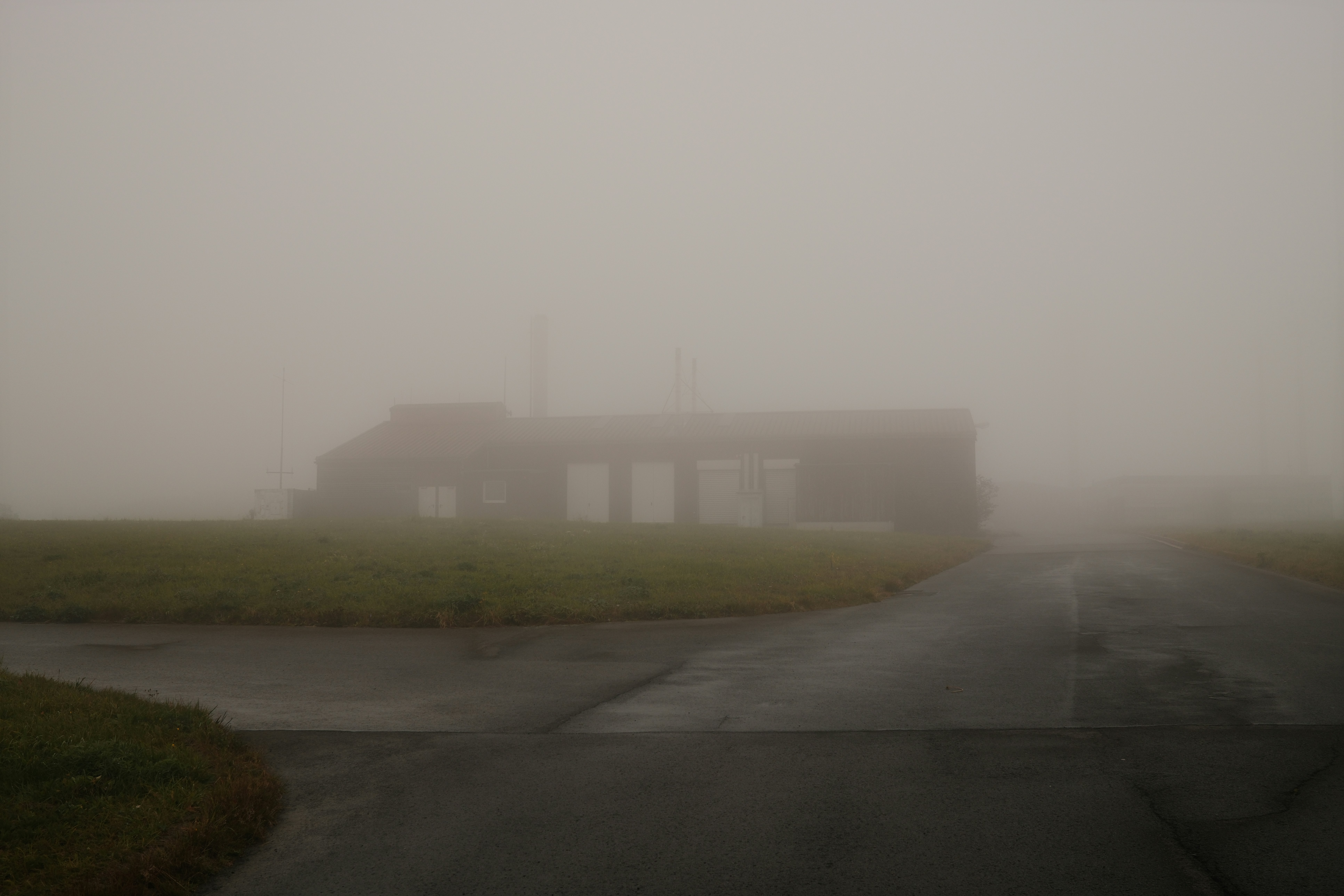 Building structure in dense fog with grassy field.