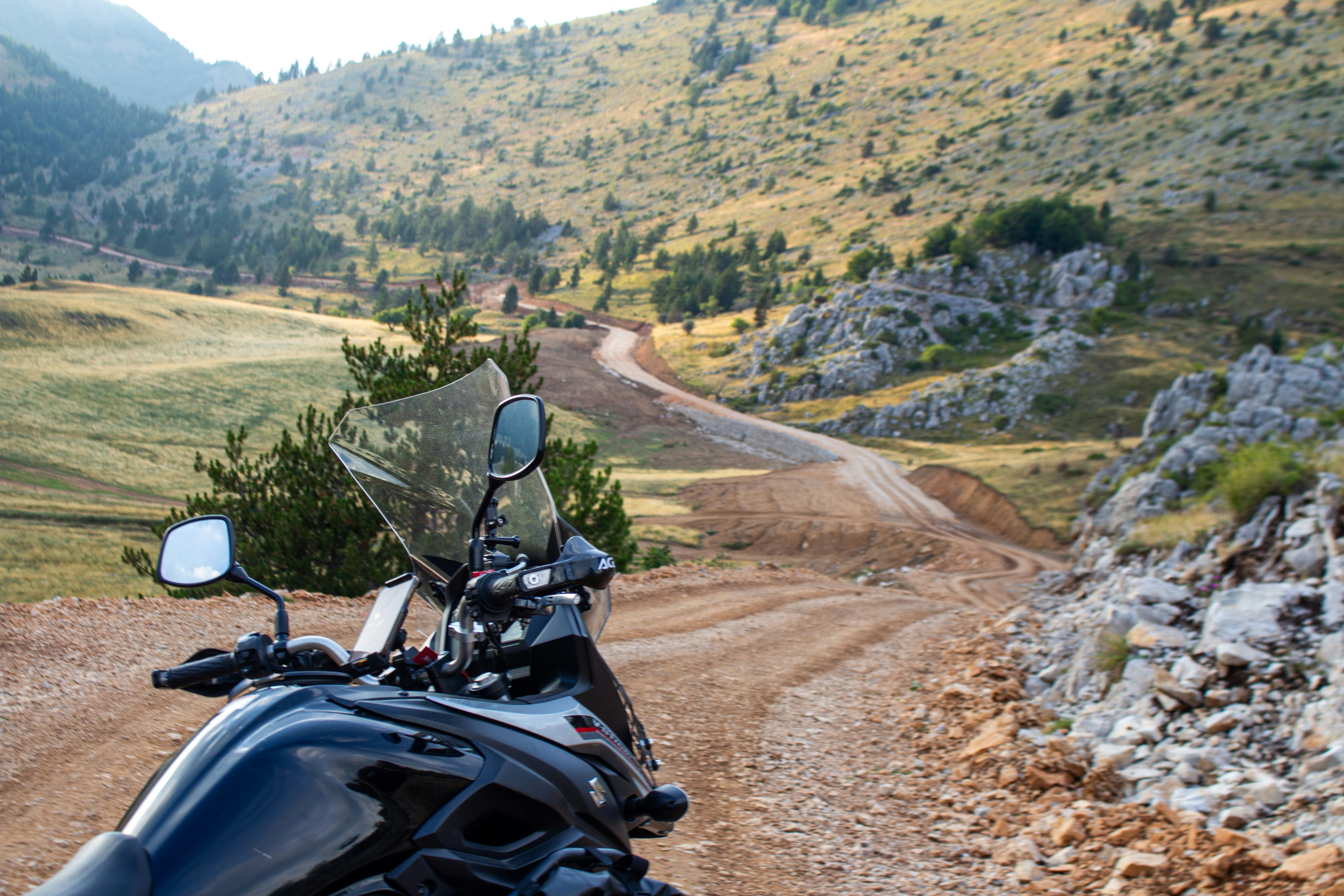 Motorcycle parked on a winding dirt road in mountains.