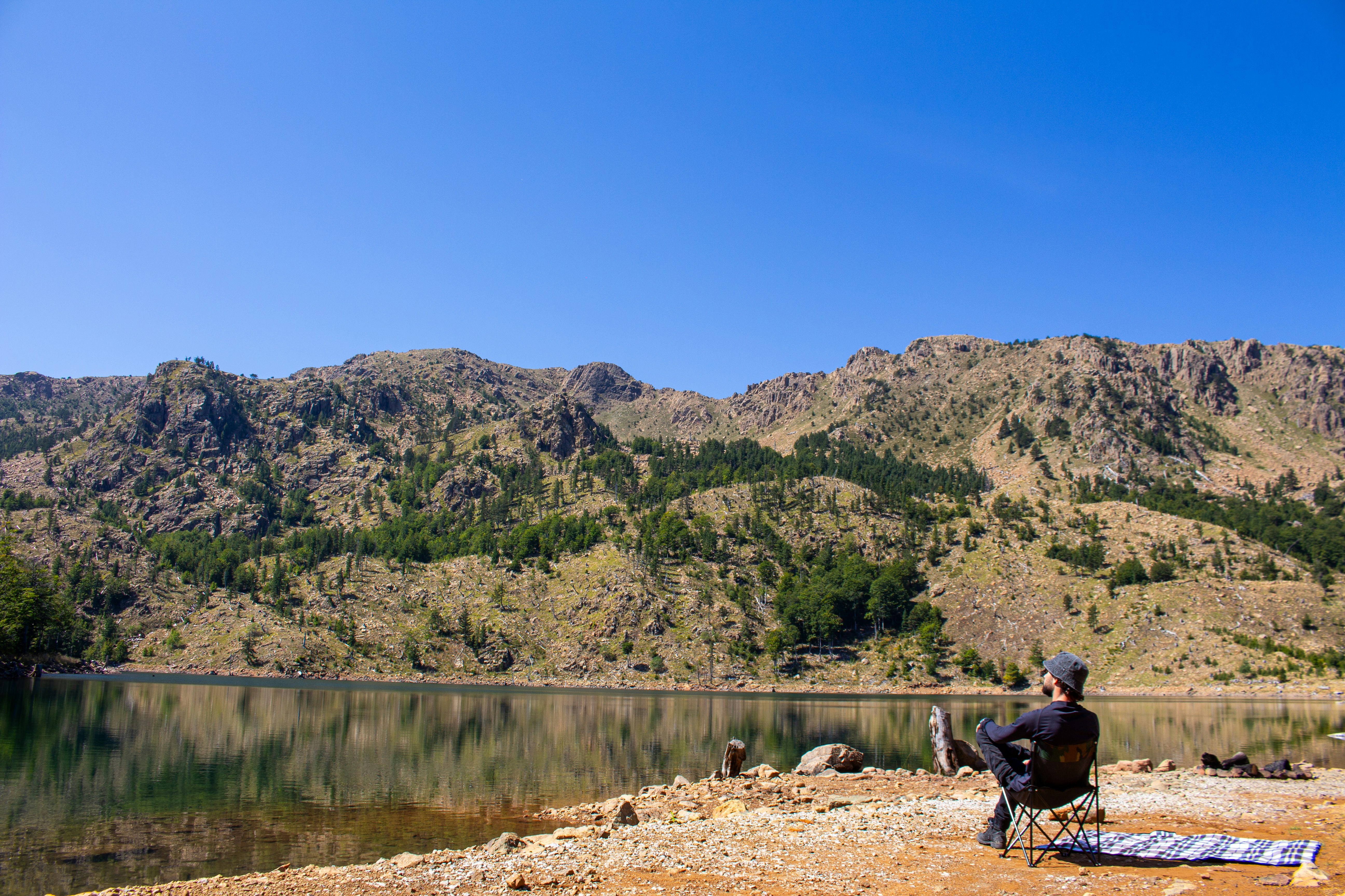 Person sitting by a lake with mountains behind.