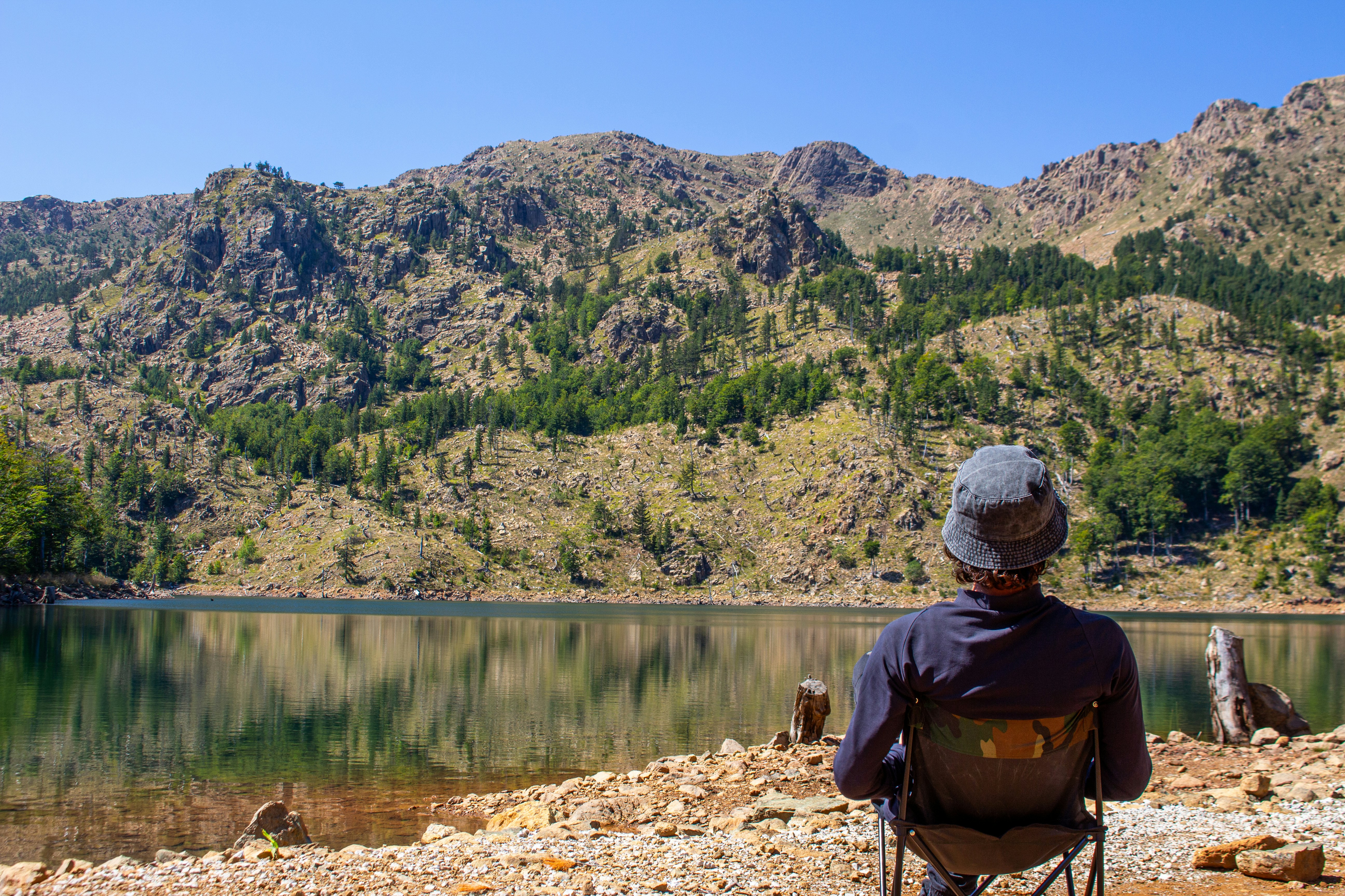 Person sitting by a lake with mountains behind.