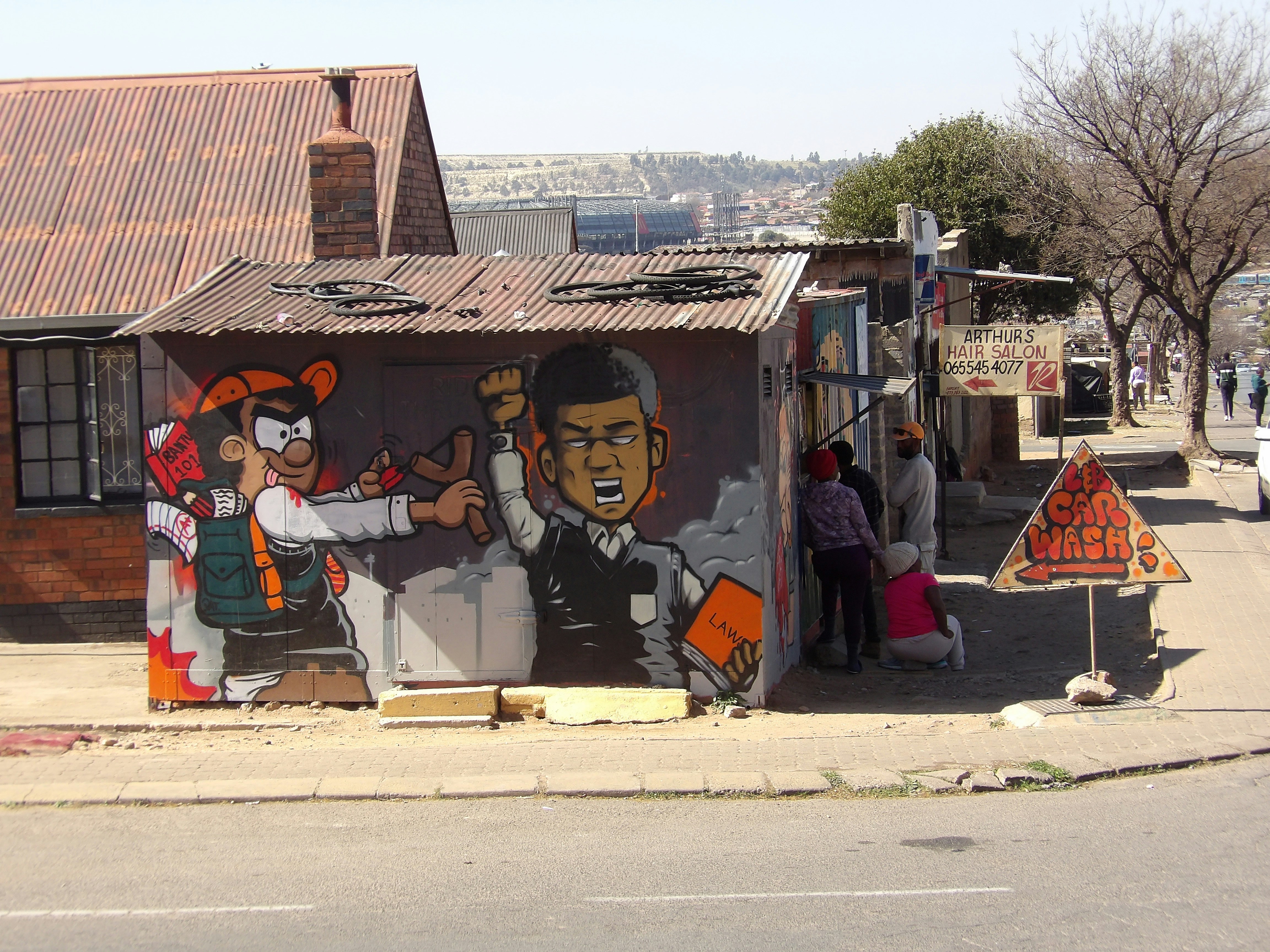 Graffiti art on a corrugated iron shack with people nearby.