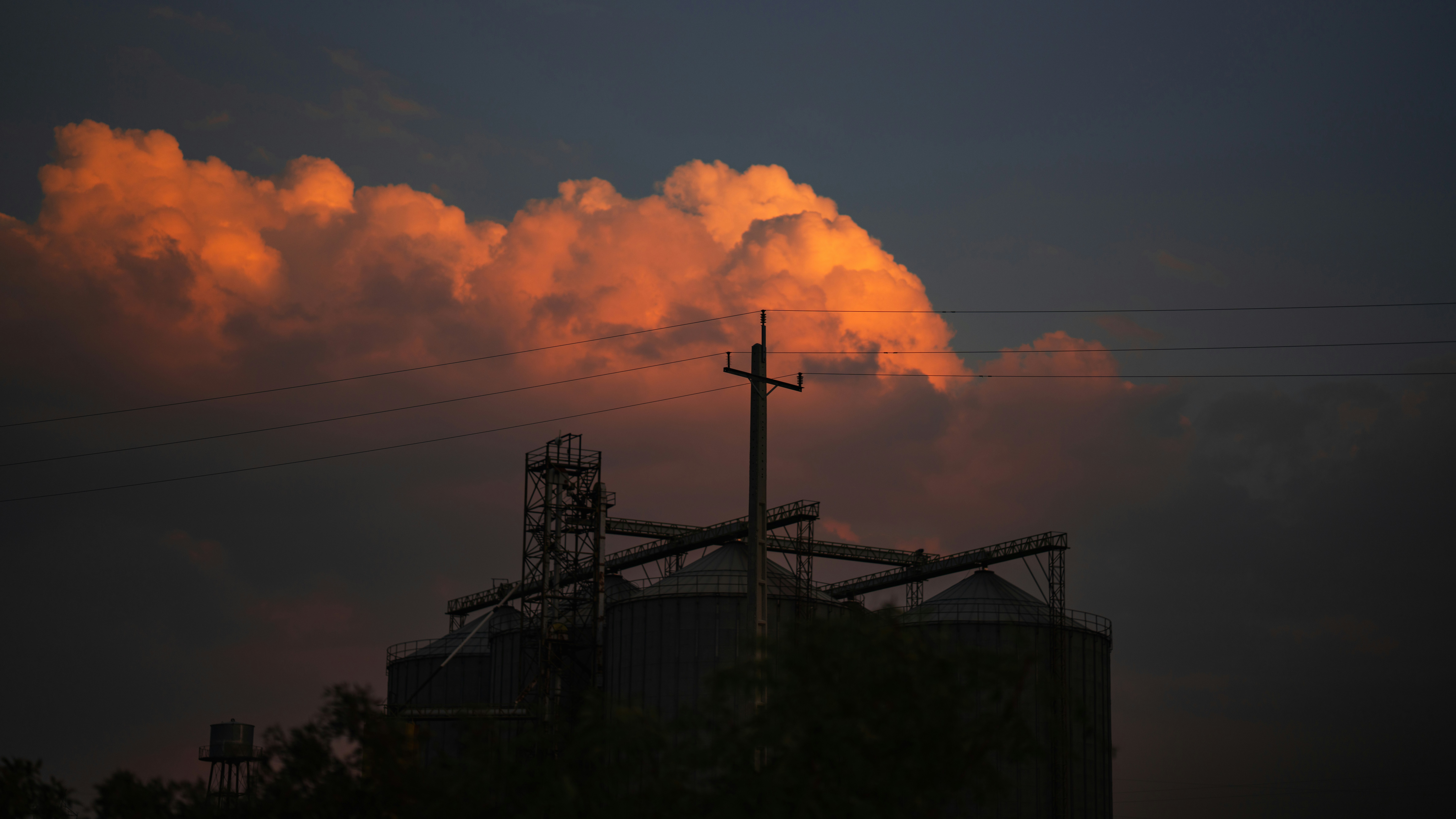 Silos industriali che si stagliano contro le drammatiche nuvole del tramonto