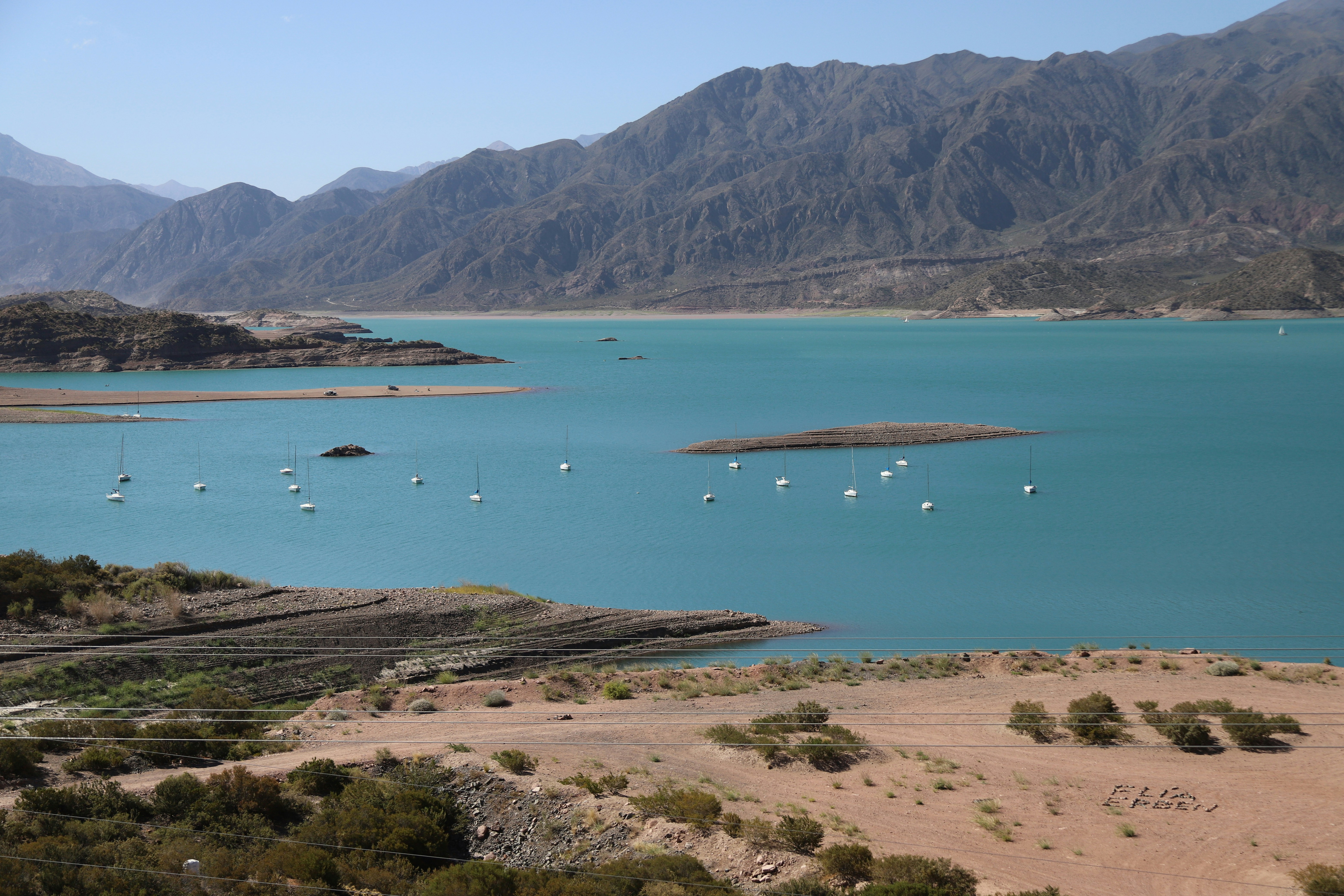 Boats sail on a bright turquoise lake near mountains.