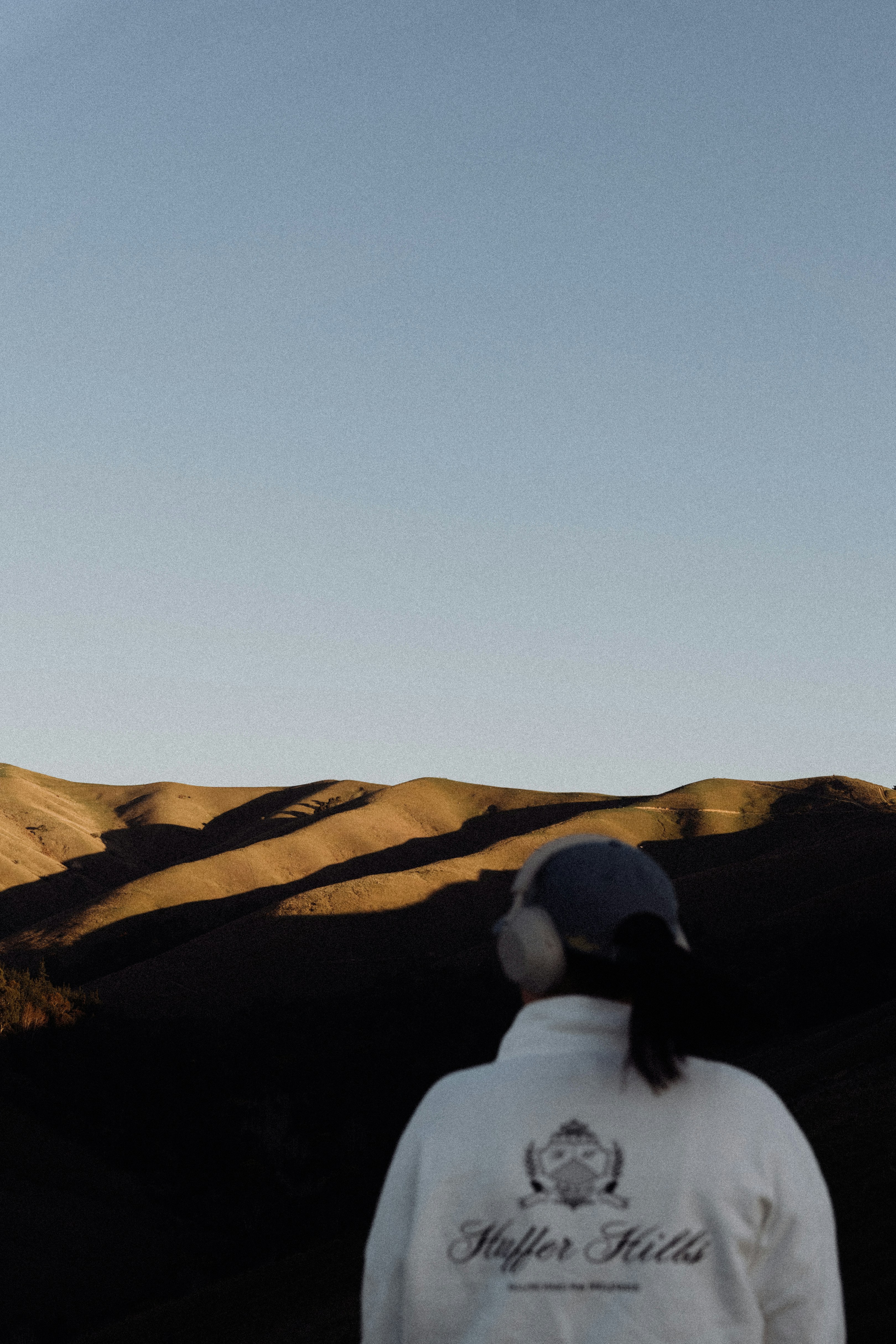 Person wearing headphones looks at rolling hills at sunset.