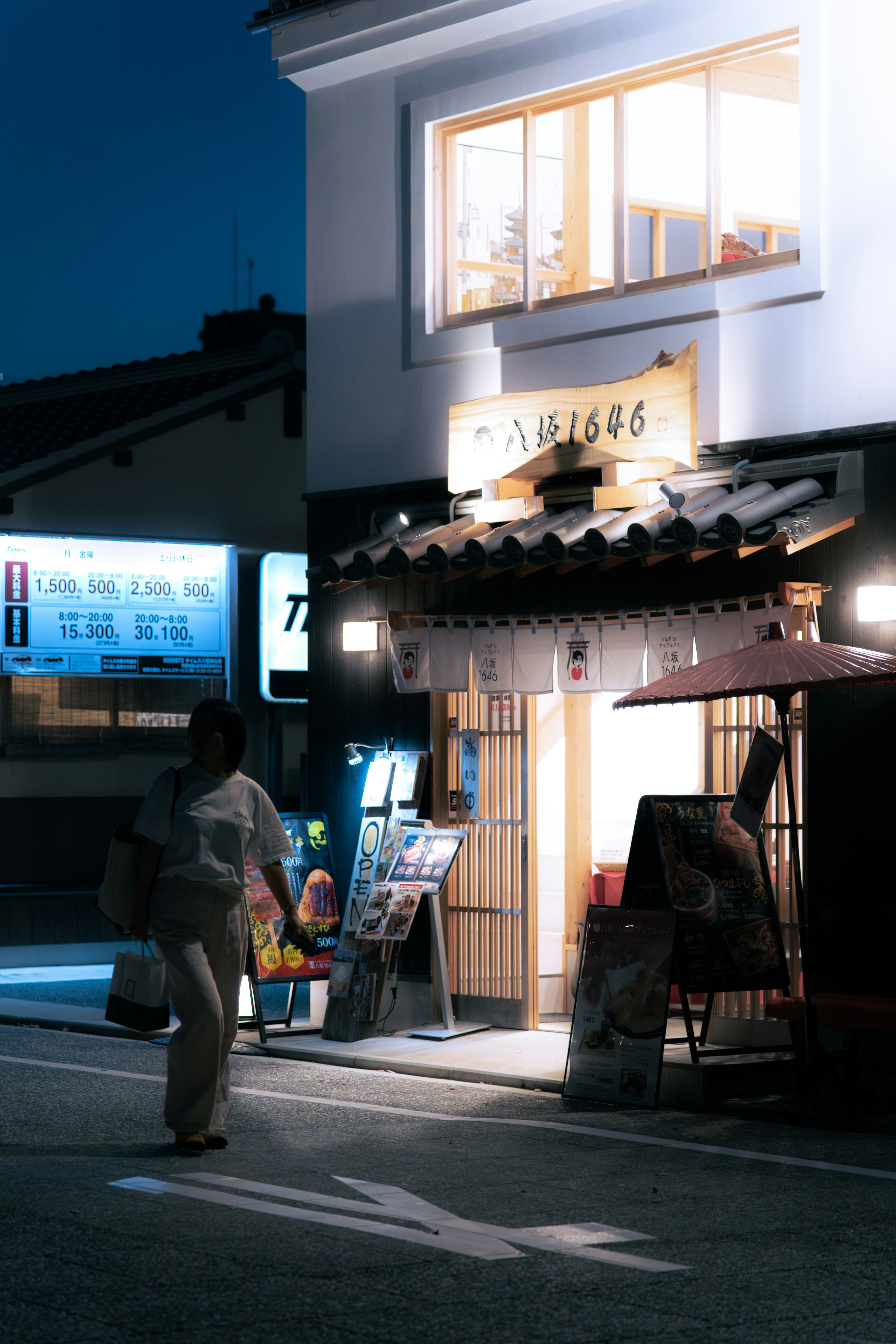 Woman walks past illuminated shop at dusk