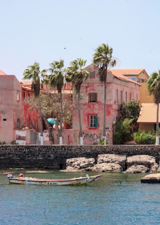 Pink building with palm trees and boat on water.