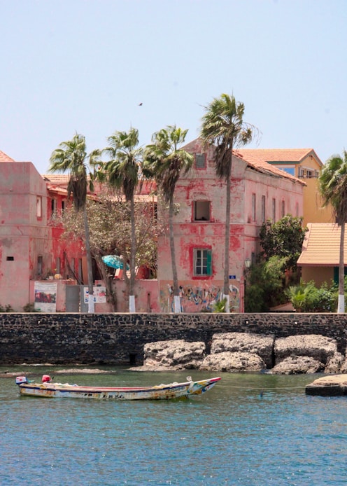 Pink building with palm trees and boat on water.
