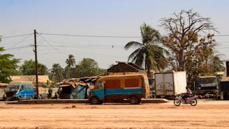 Motorcyclist rides past parked vehicles and buildings.