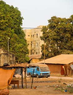Blue truck parked near buildings with trees.