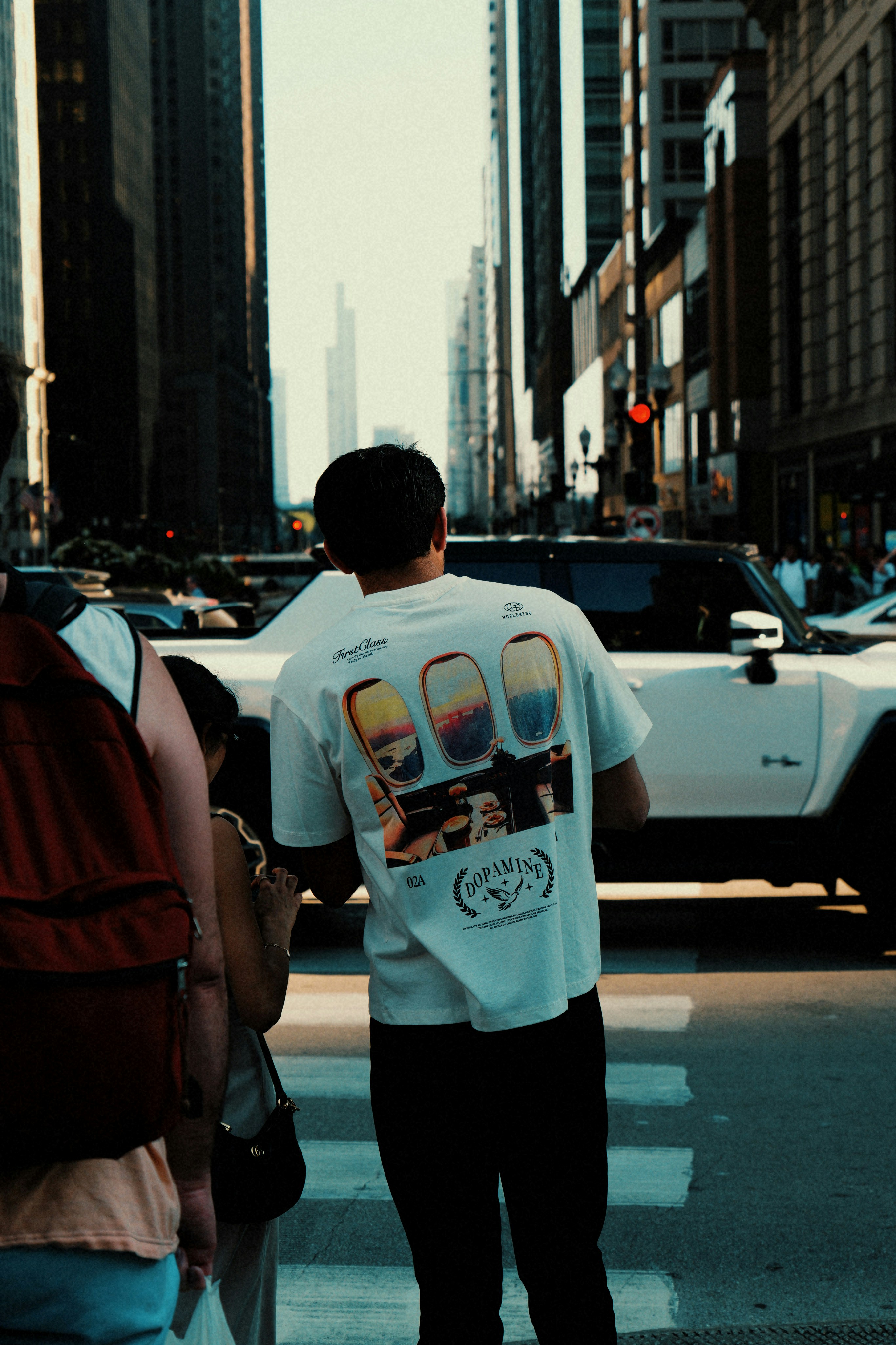 Man wearing t-shirt with airplane window scenes crosses street.