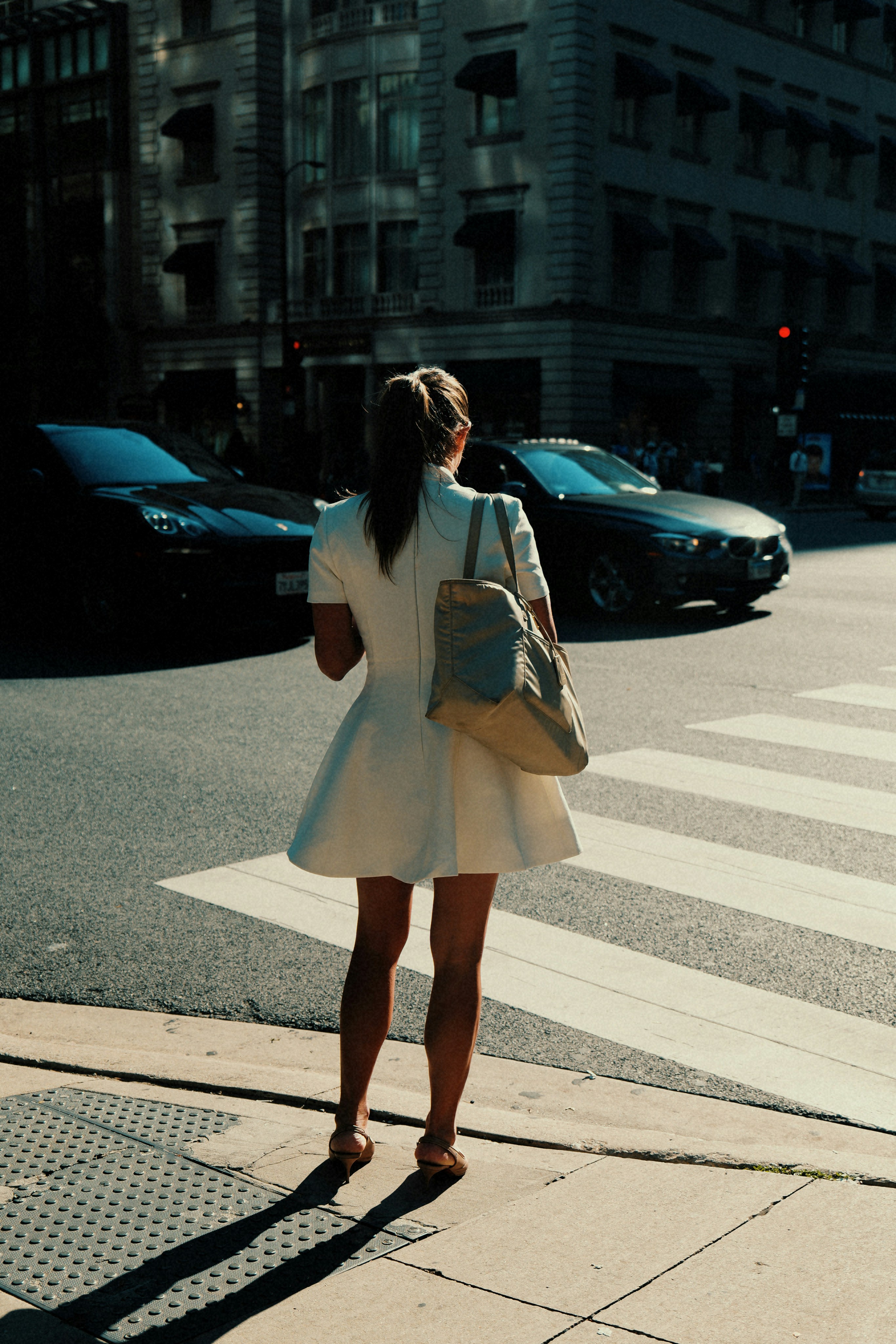 Woman in white dress waits at a crosswalk