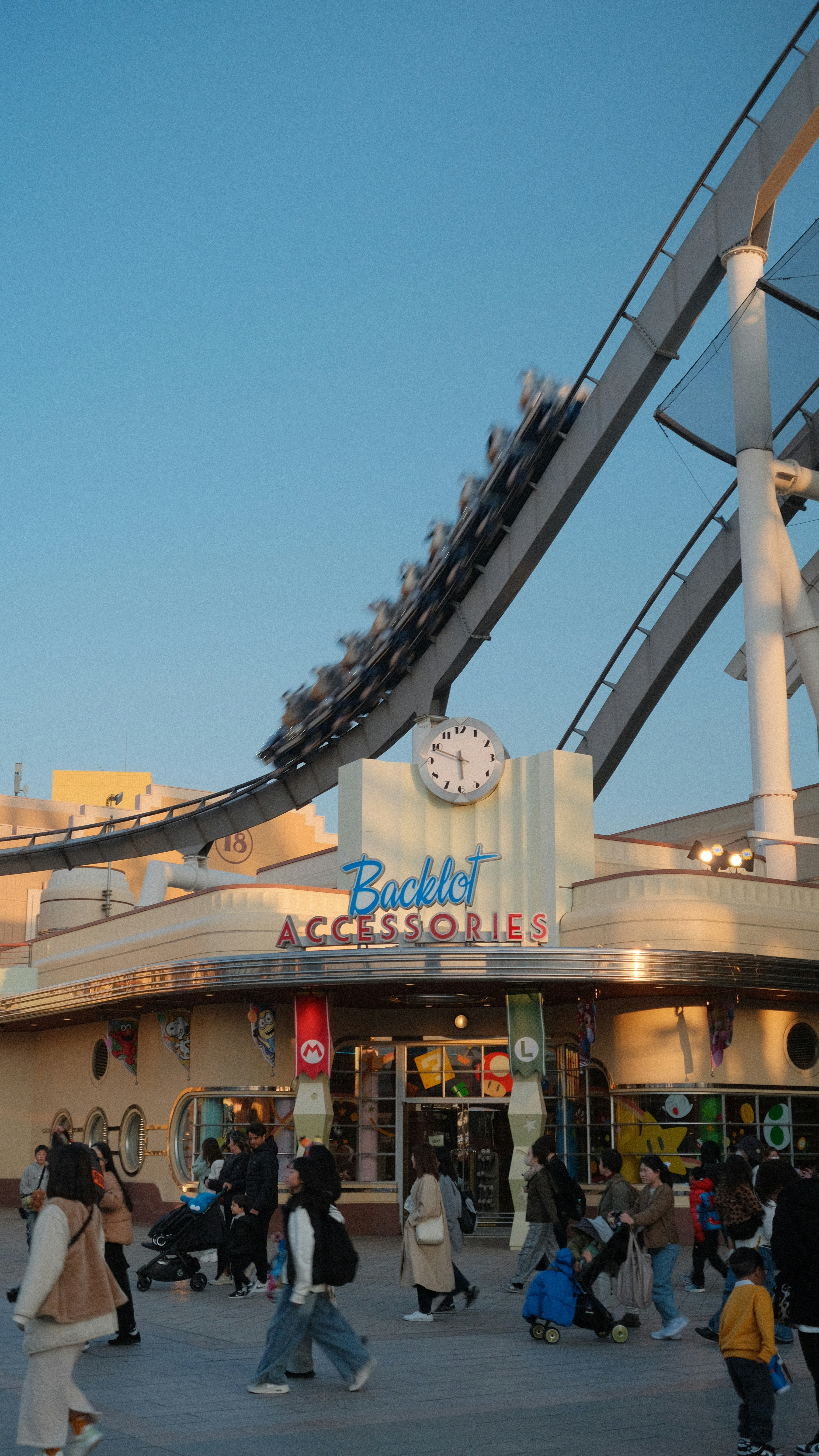 Roller coaster train ascends above a busy street with shops.