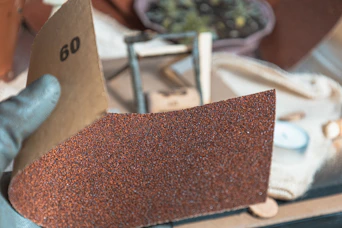 Gloved hand holding sandpaper with grit number 60.