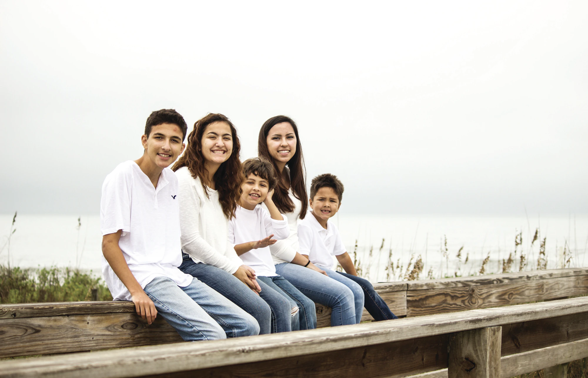 A smiling family sitting together on a boardwalk by the ocean