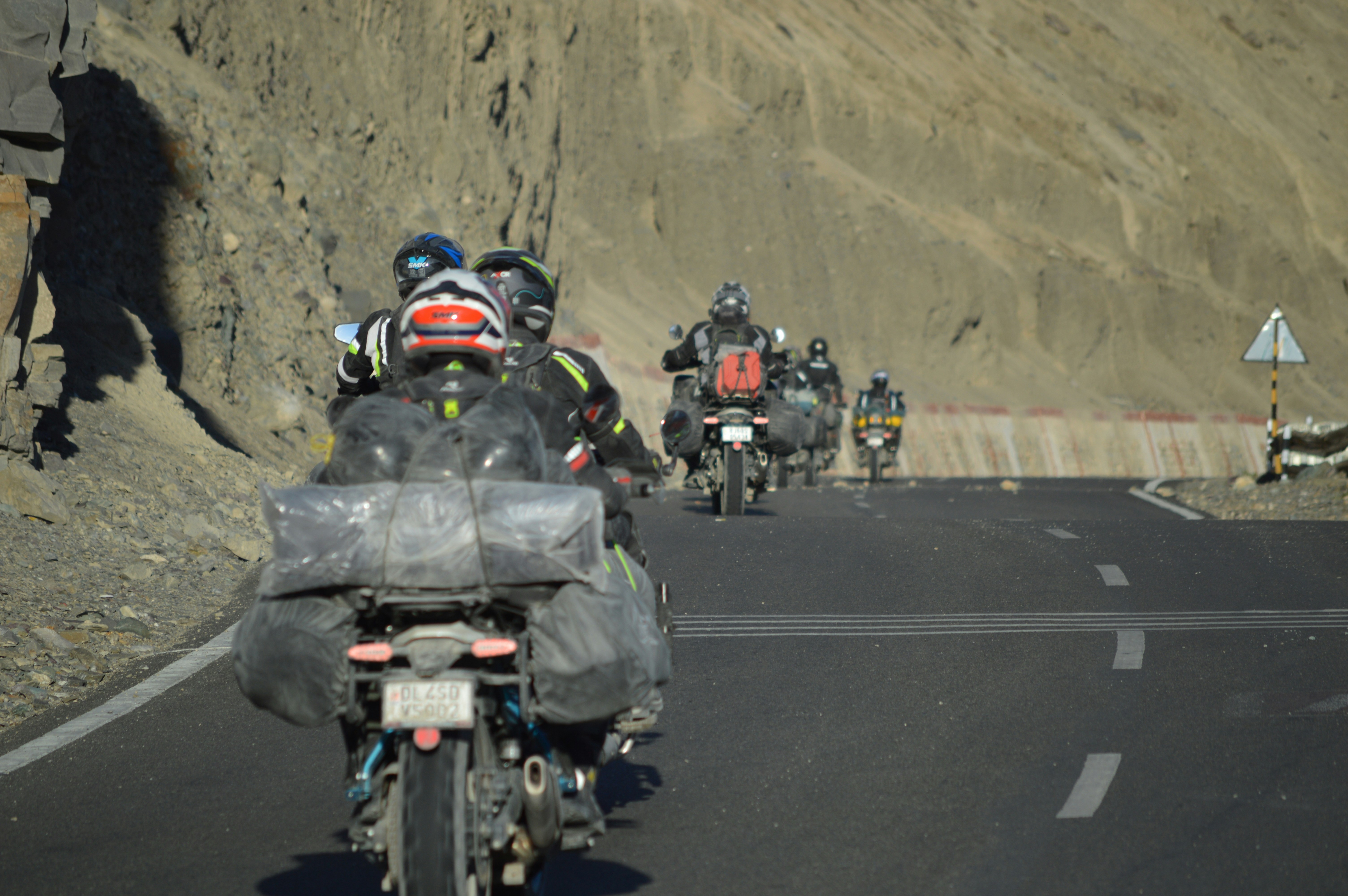 Motorcyclists ride on a paved road through mountains.
