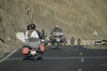 Motorcyclists ride on a paved road through mountains.