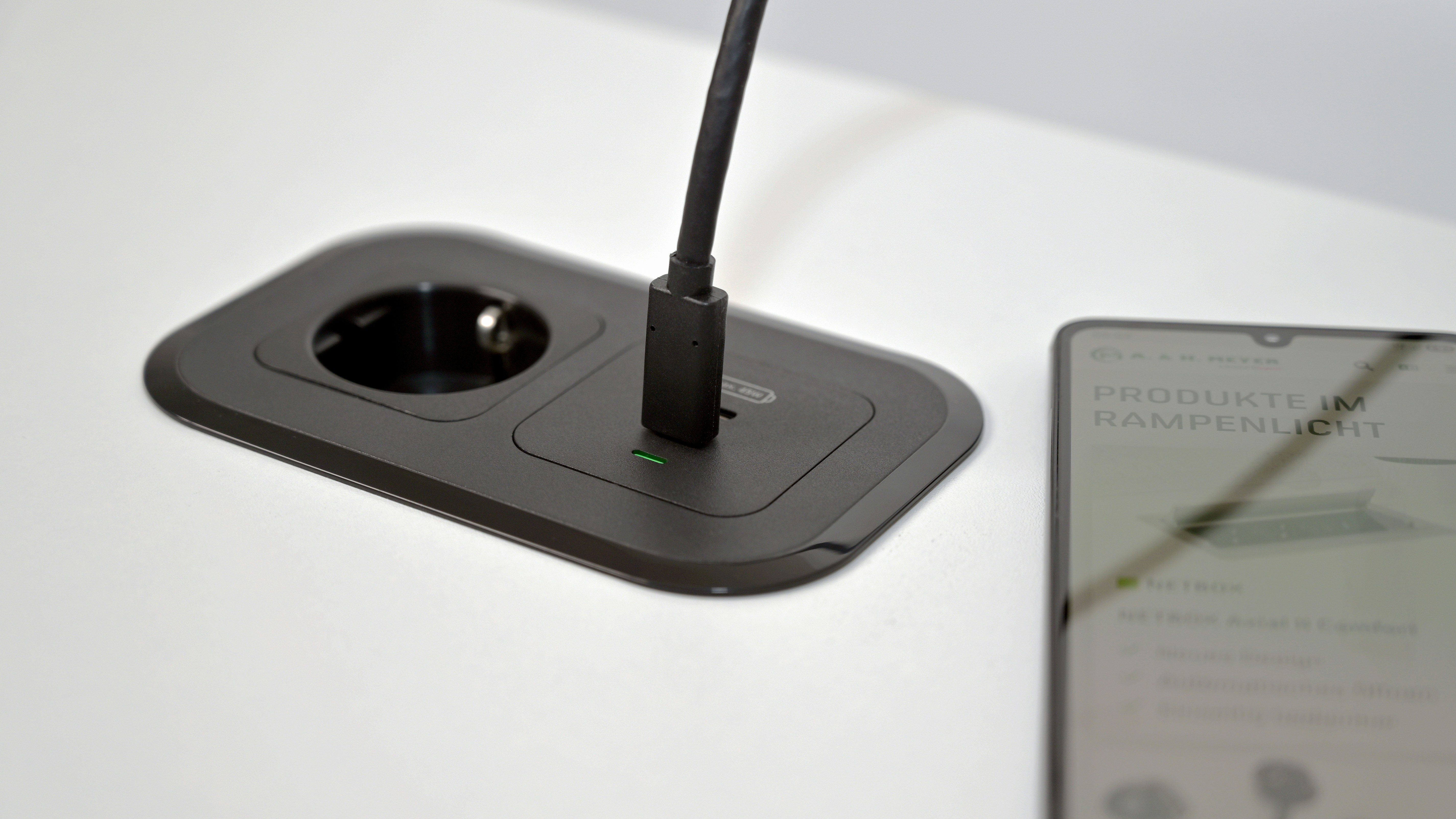 Kabelloses Ladegerät mit USB-C-Anschluss und Steckdose auf dem Schreibtisch.