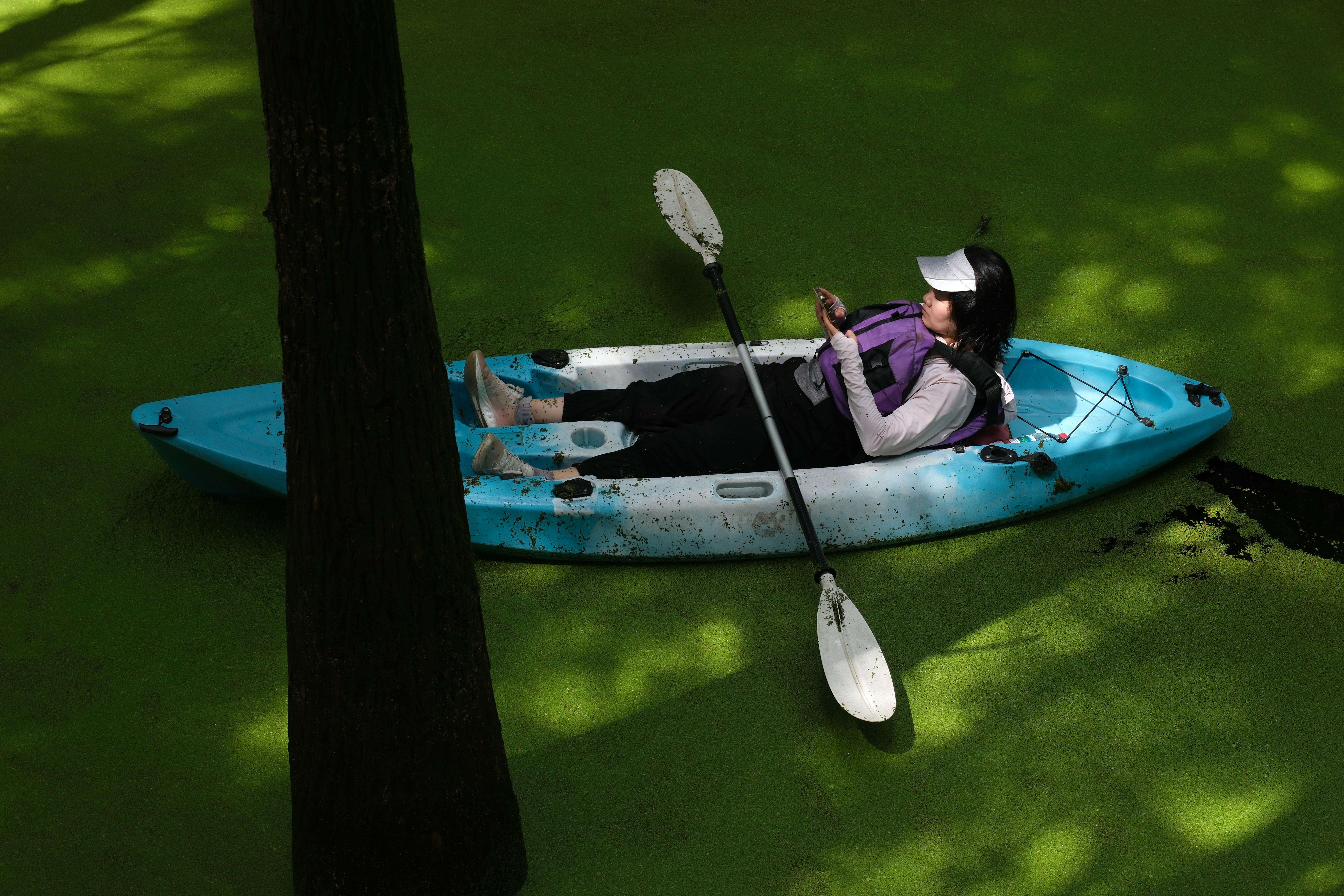 Frau im Kajak auf grünem Wasser mit Telefon