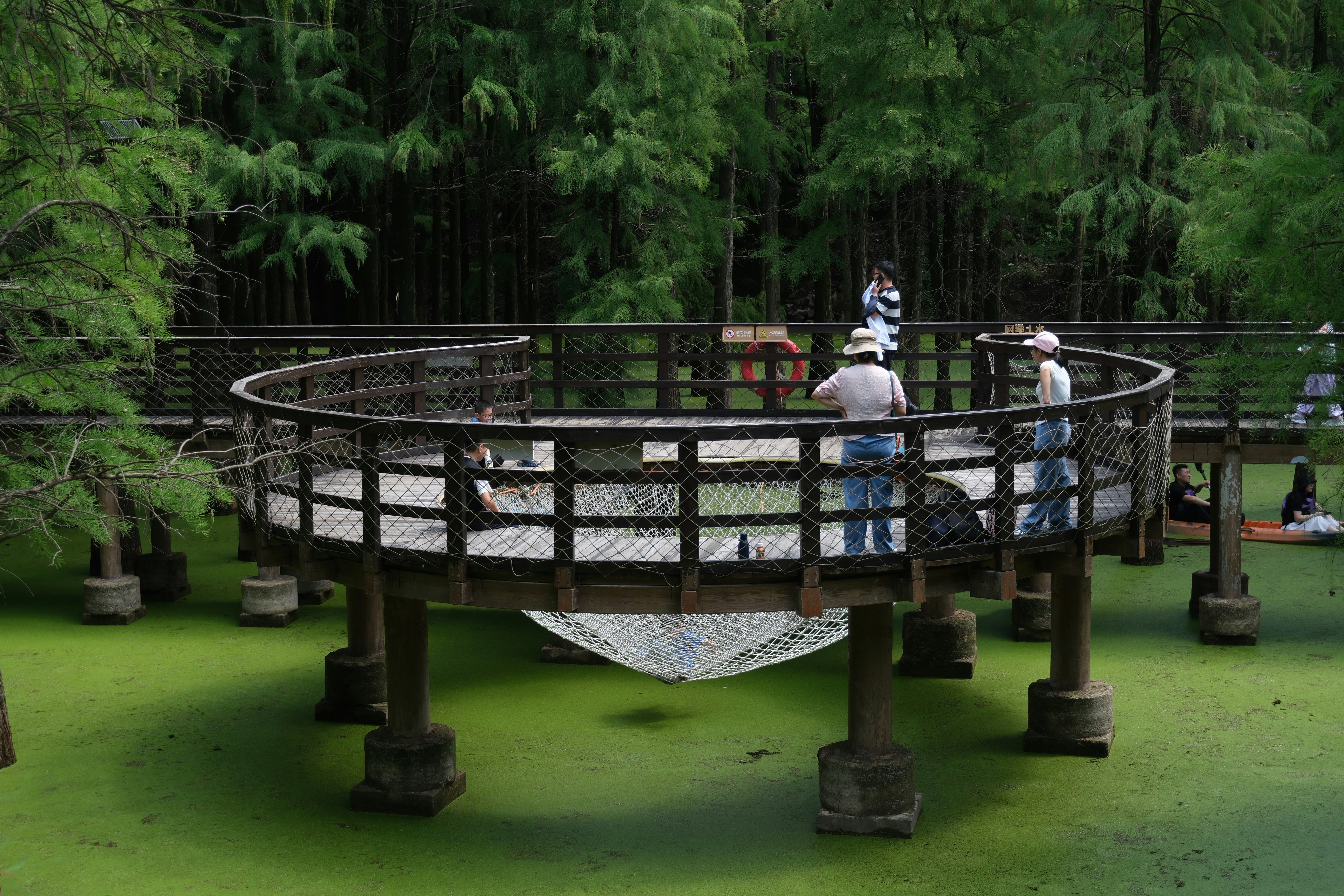 Menschen auf einer kreisförmigen Holzterrasse, umgeben von grünem Wasser