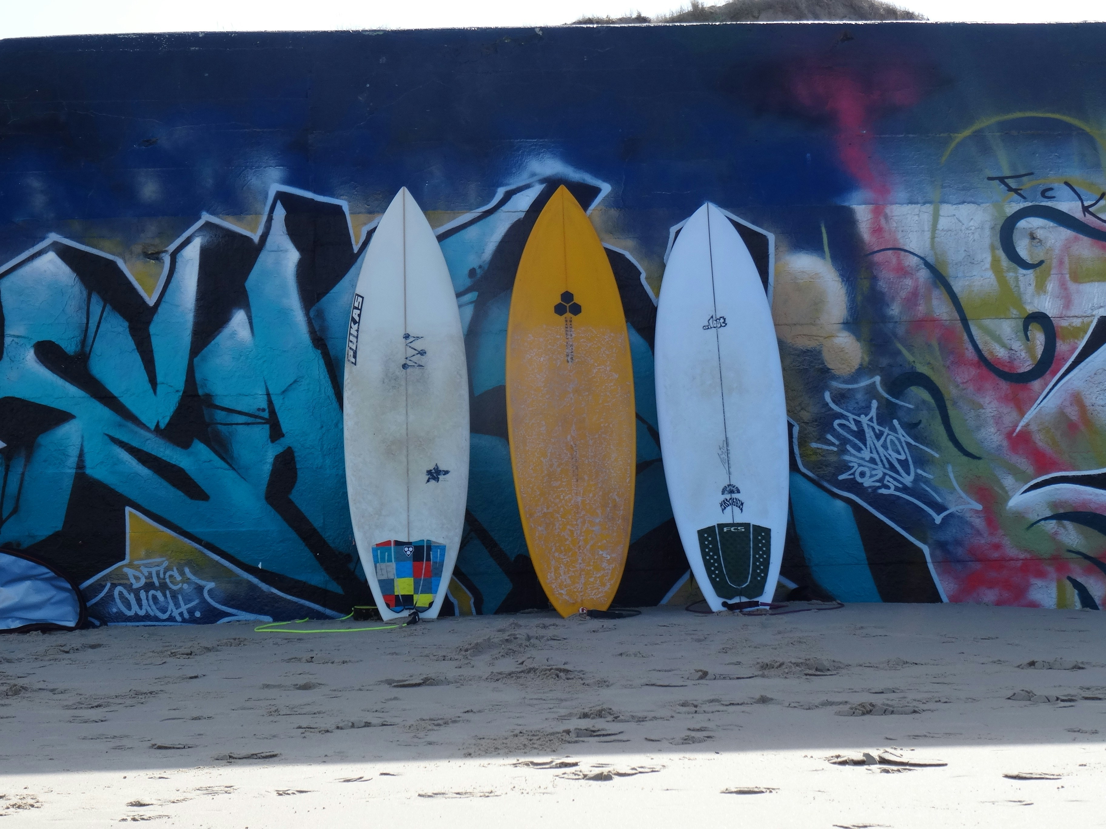 Drei Surfbretter lehnen an einer Graffiti-Wand.