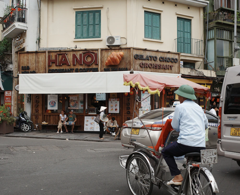 A cyclo driver passes a busy corner cafe