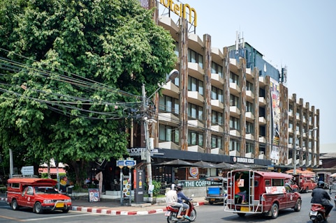 Red tuk-tuks drive past a modern building.