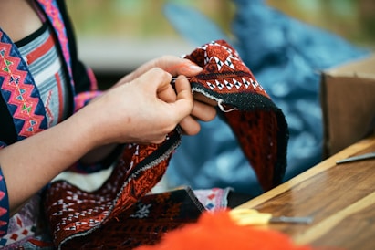 Hands sewing intricate patterned textile with needle.