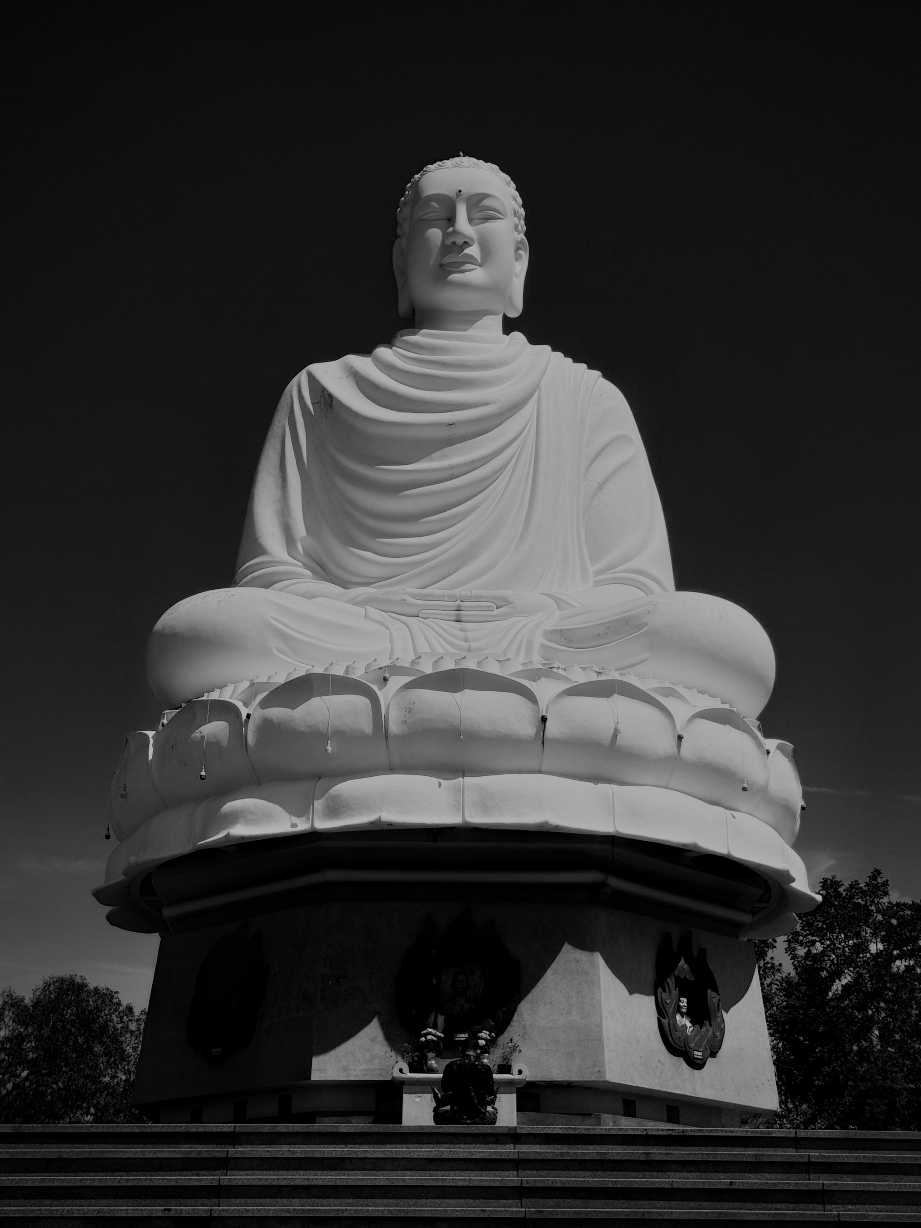 Large white buddha statue seated on lotus flower pedestal.