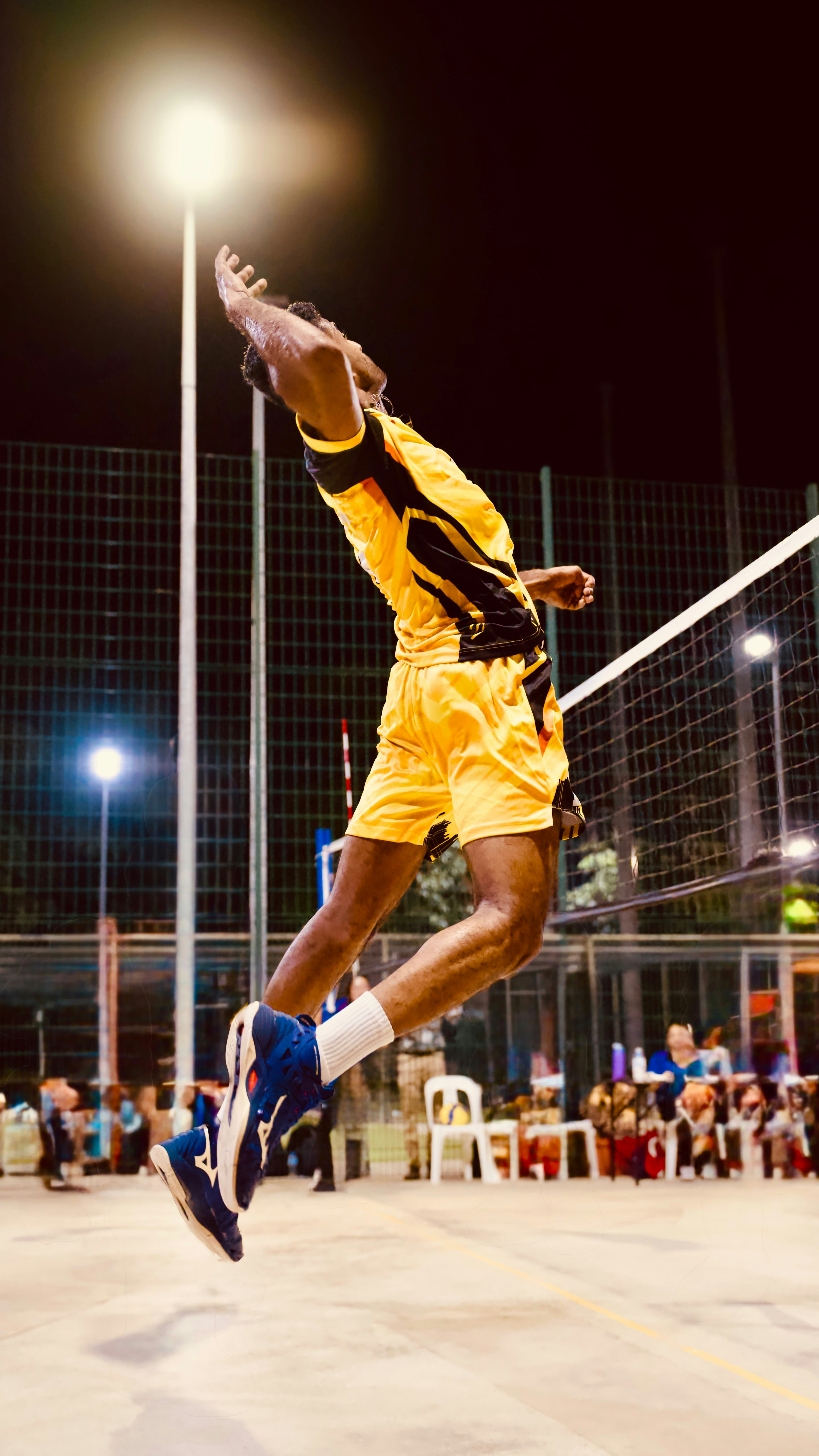Volleyball player jumping to spike the ball at night.
