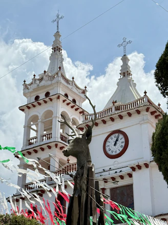 White church with clock tower and deer sculpture