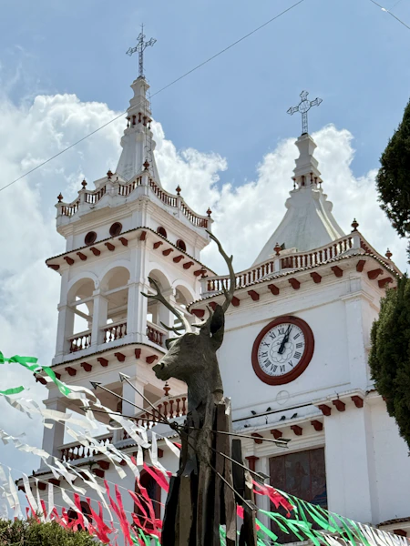 White church with clock tower and deer sculpture