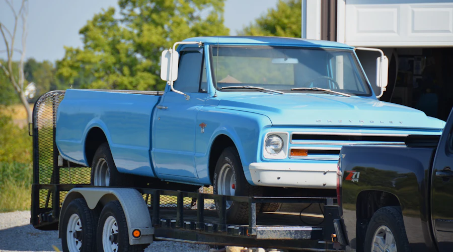 A light blue classic pickup truck strapped down on a flatbed trailer