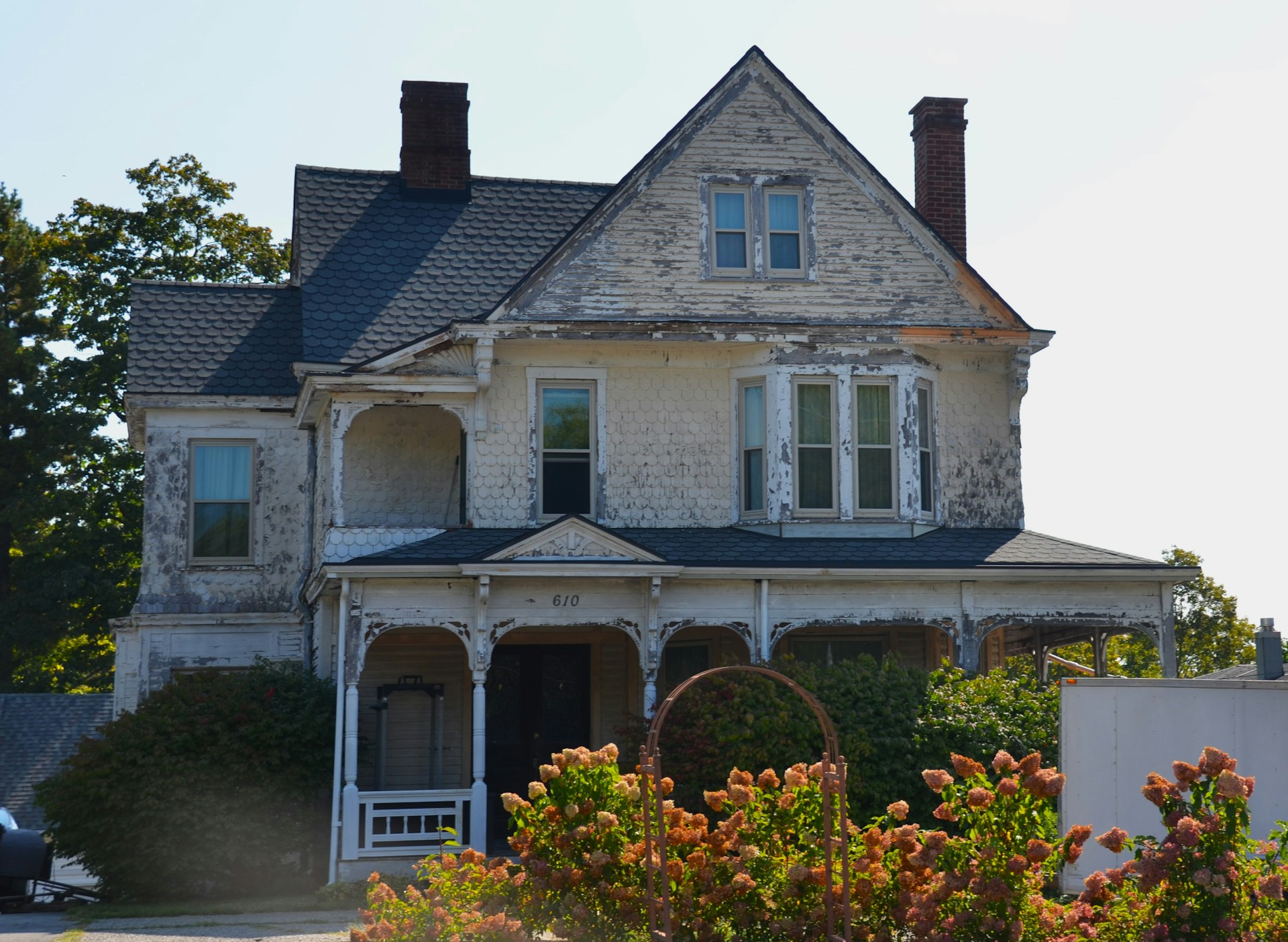 Old weathered house with peeling paint and overgrown bushes.