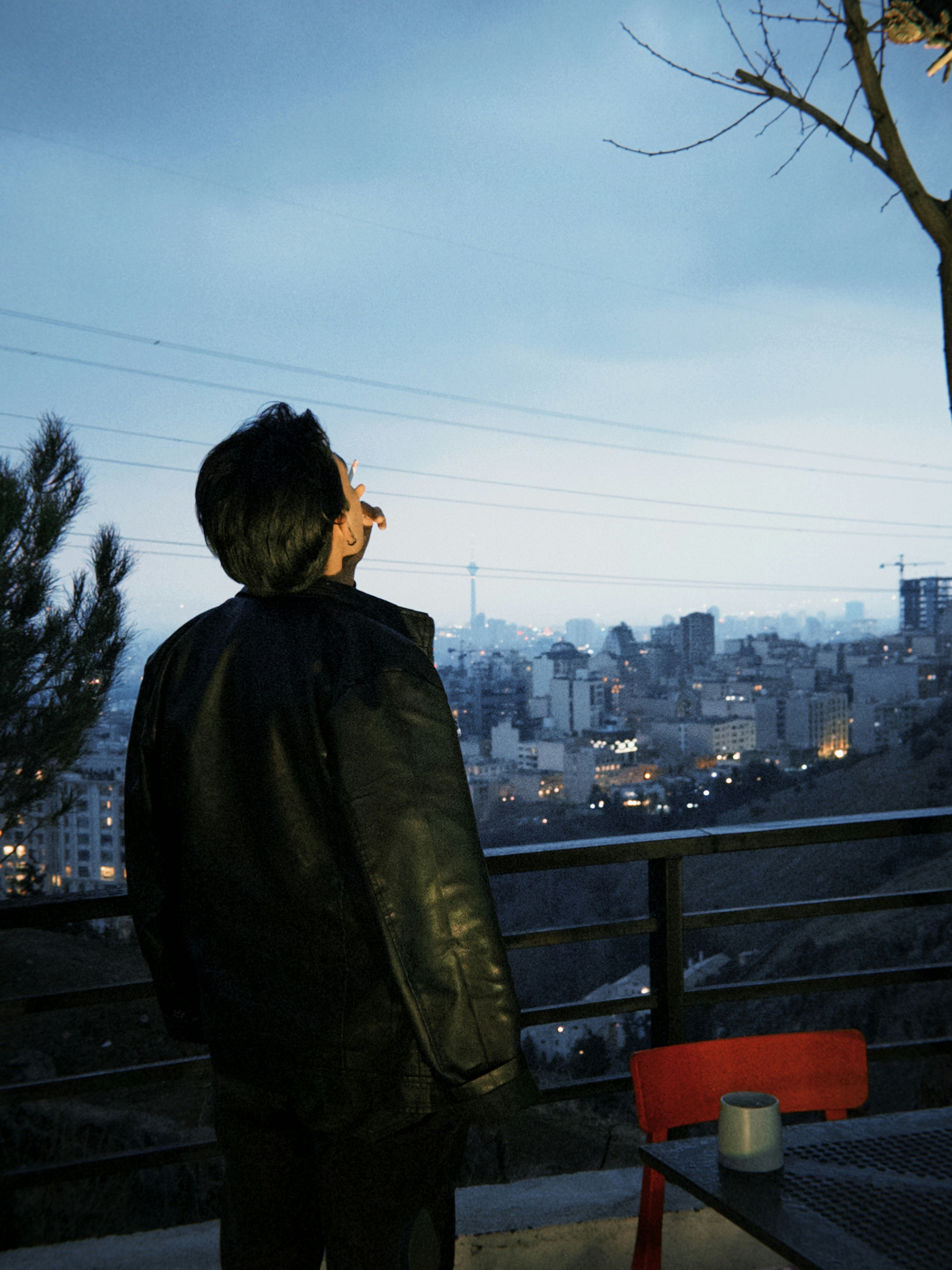 Man in leather jacket looks at city skyline at dusk.