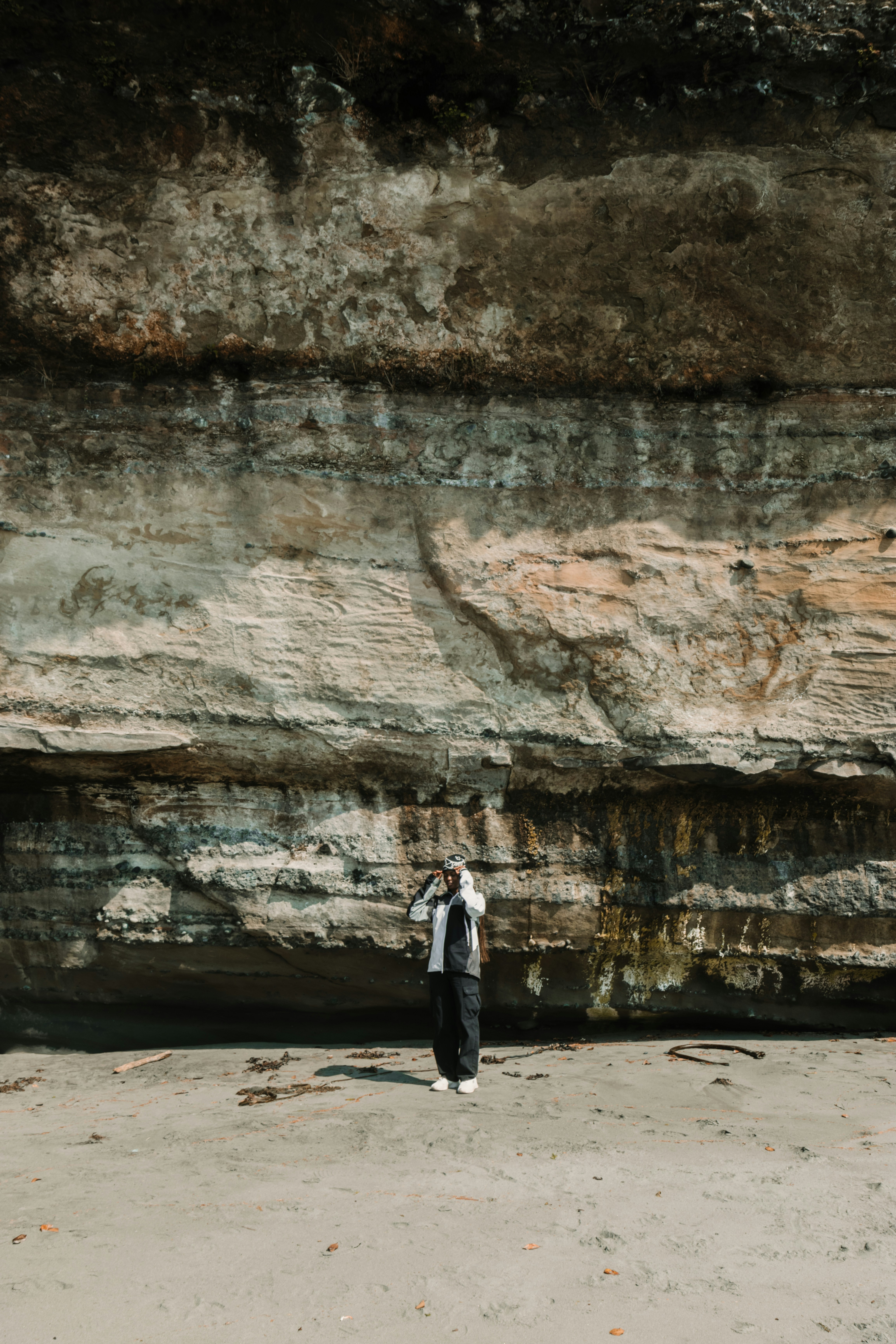 Person standing on beach below large rock formation