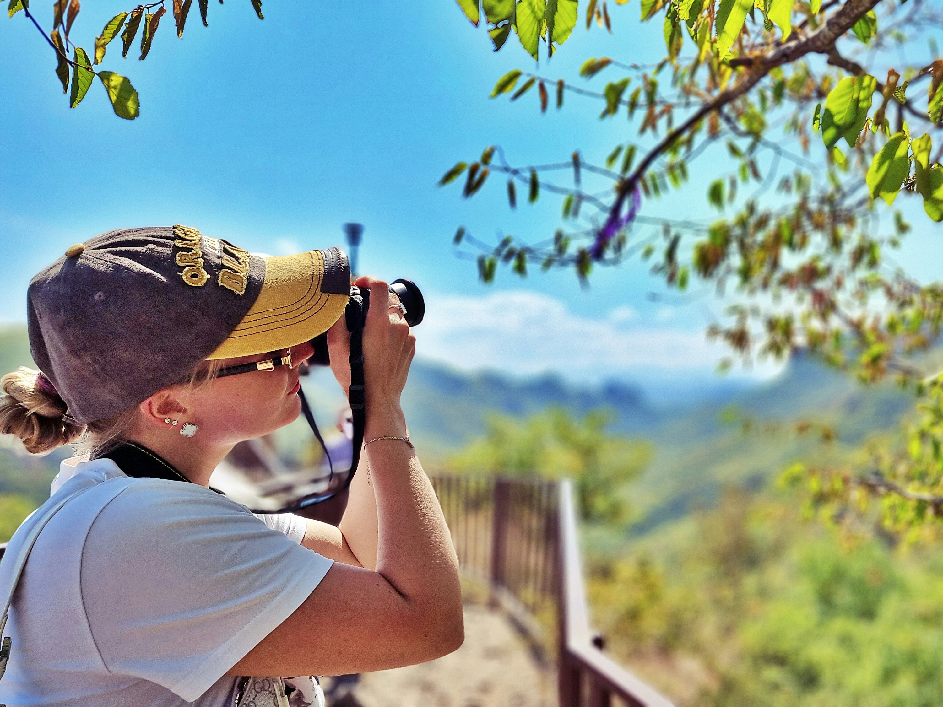 Woman with camera photographs scenic mountain landscape.
