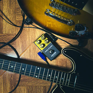 Two electric guitars and a pedal on wooden floor