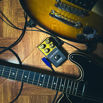 Two electric guitars and a pedal on wooden floor
