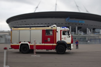 Red and white fire truck parked near modern stadium.