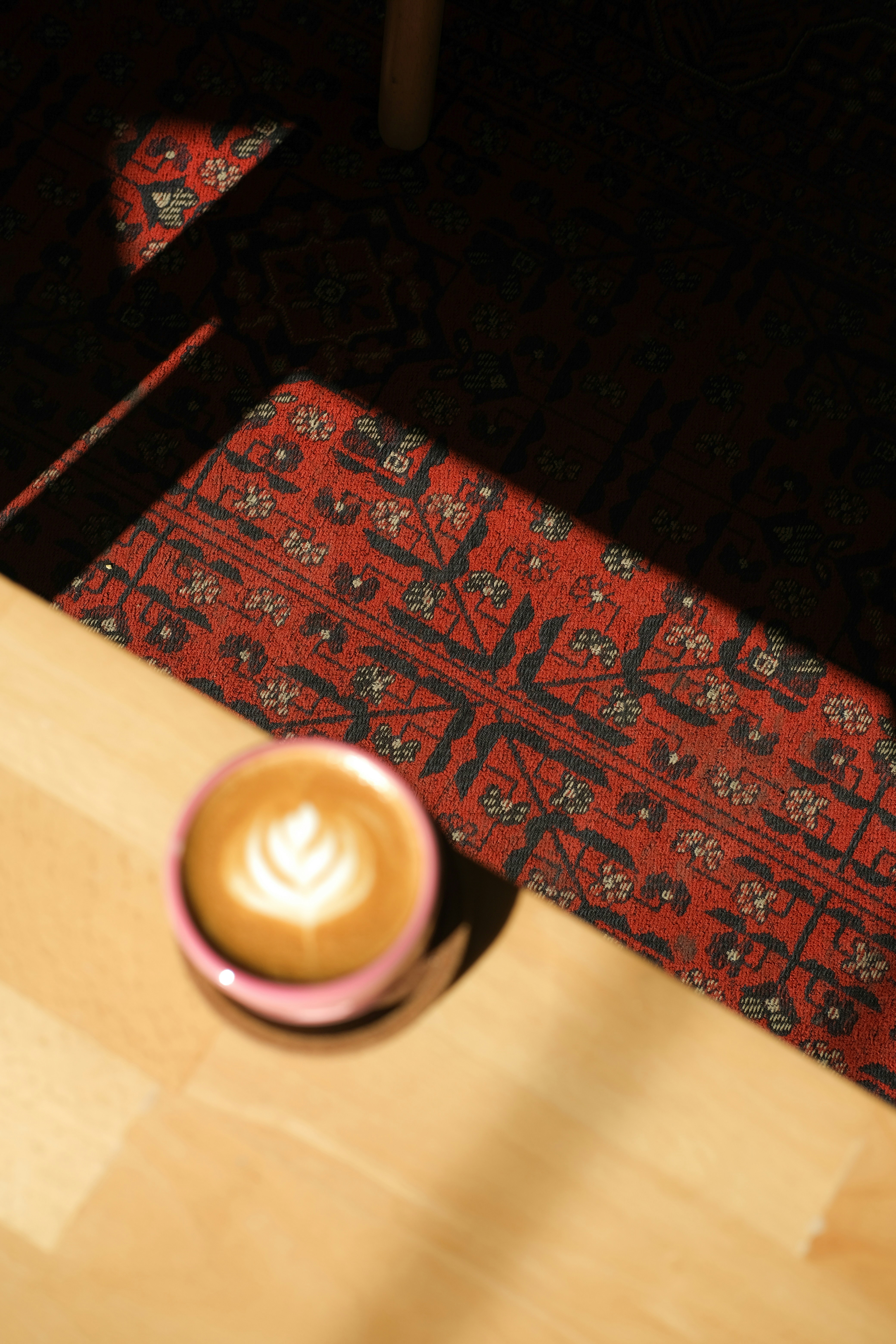 Latte Art in einem rosa Becher auf einer Holzoberfläche.