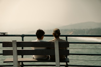 Two people sit on a bench overlooking the ocean.