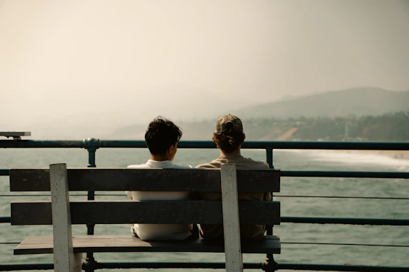 Two people sit on a bench overlooking the ocean.