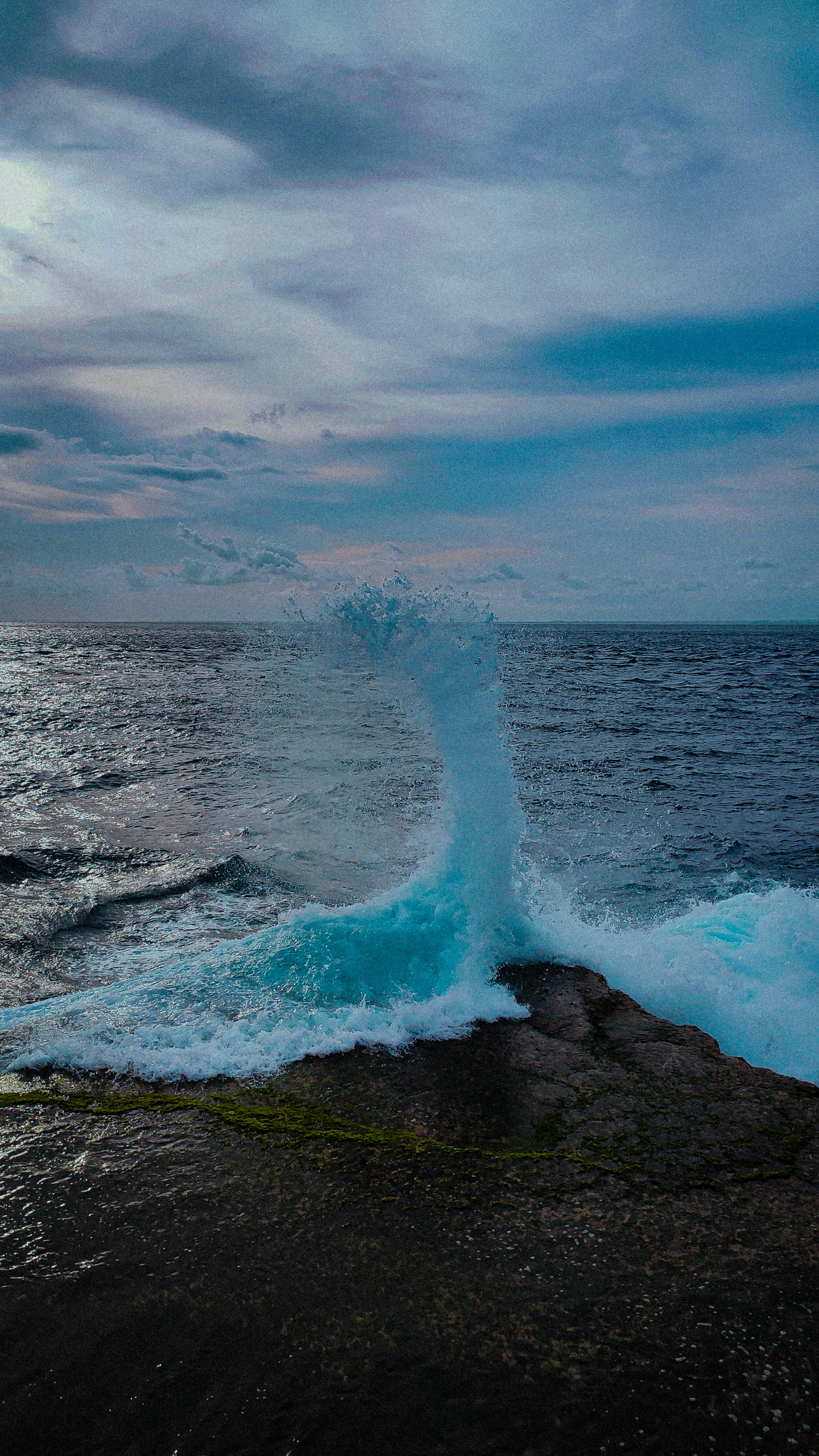 Ocean waves crash against rocky shore under cloudy sky