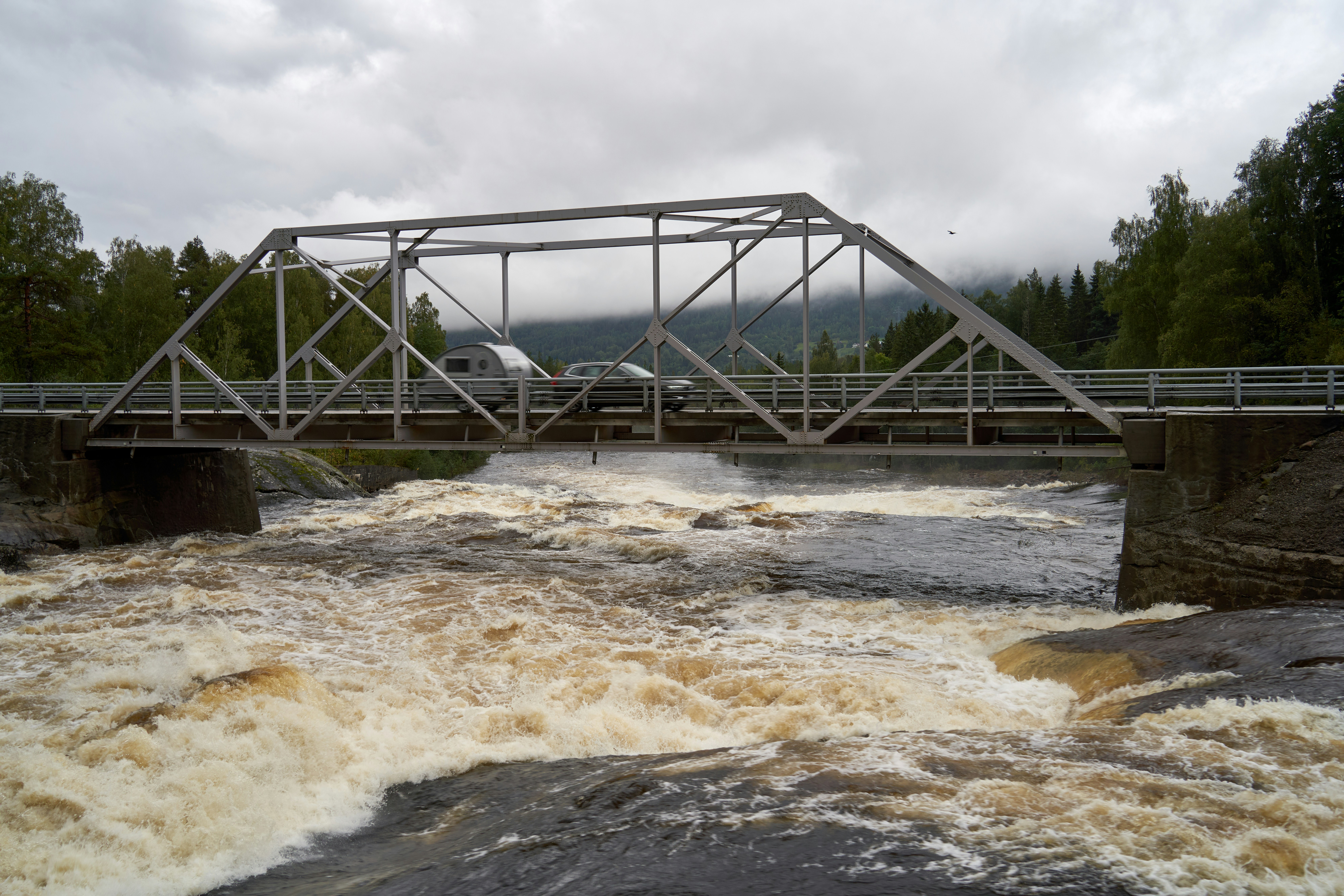 Car with caravan crossing mountain river bridge