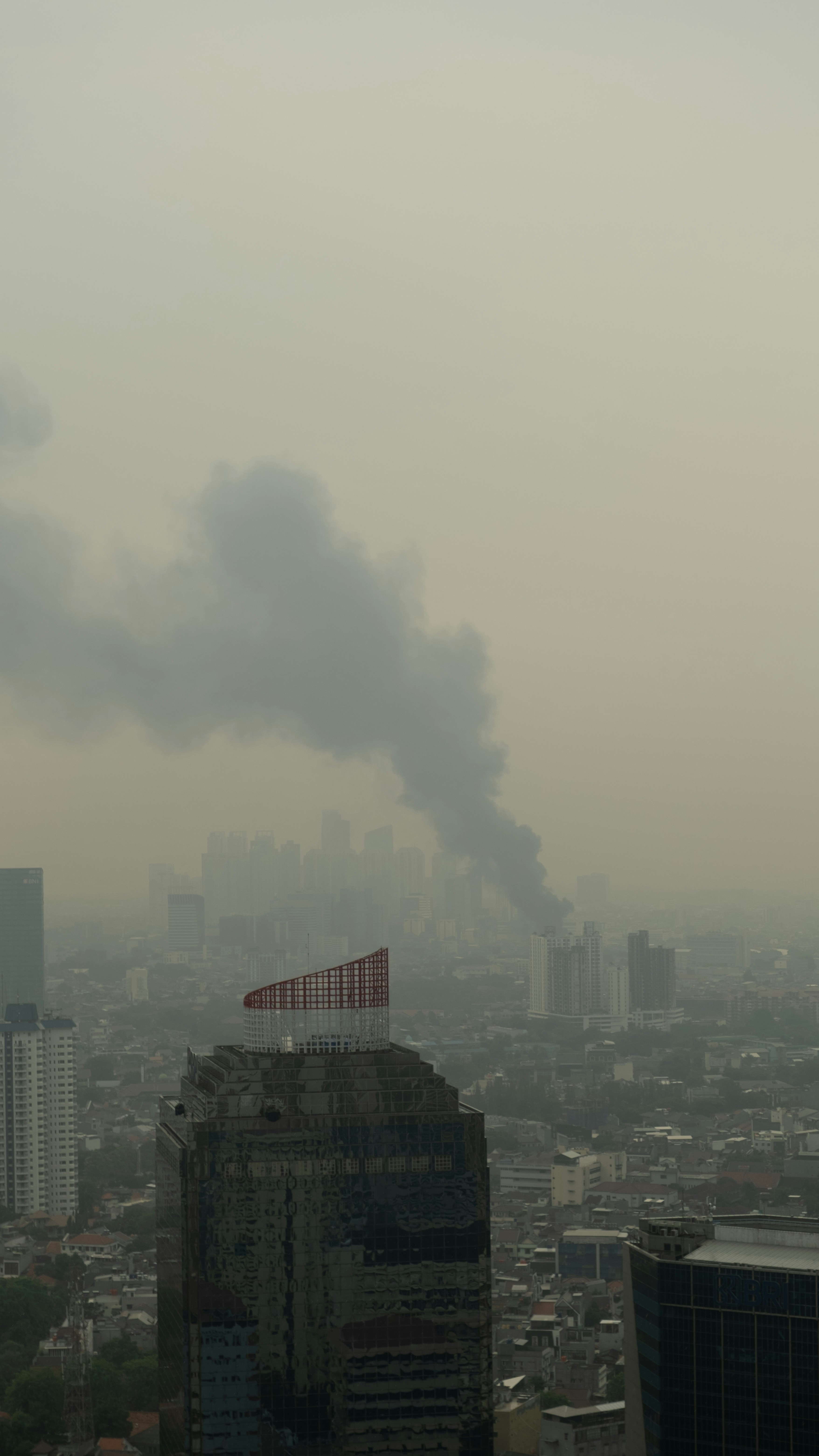 Smoke billows over a hazy cityscape with skyscrapers.