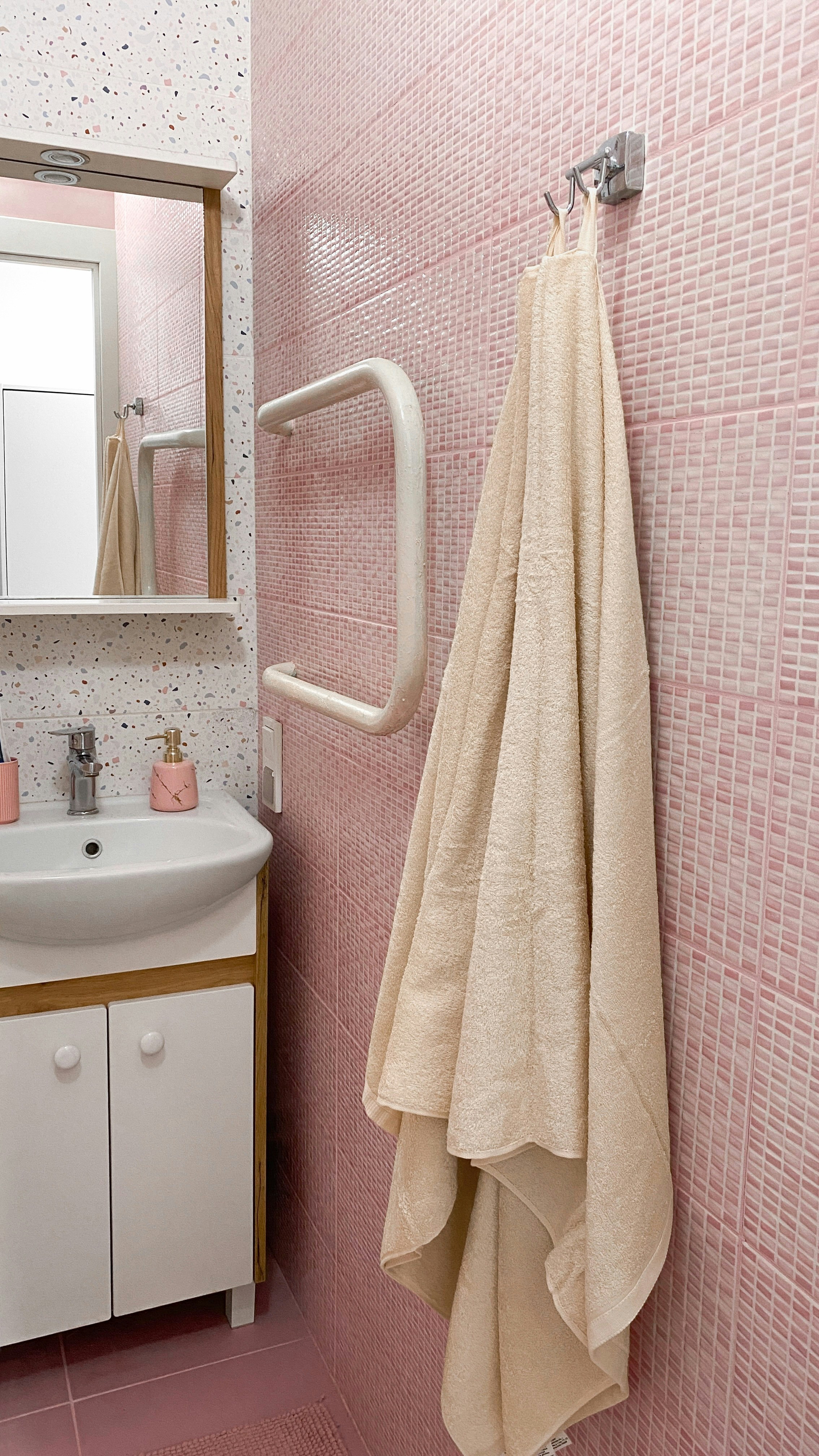 A beige towel hangs on a pink tiled bathroom wall.