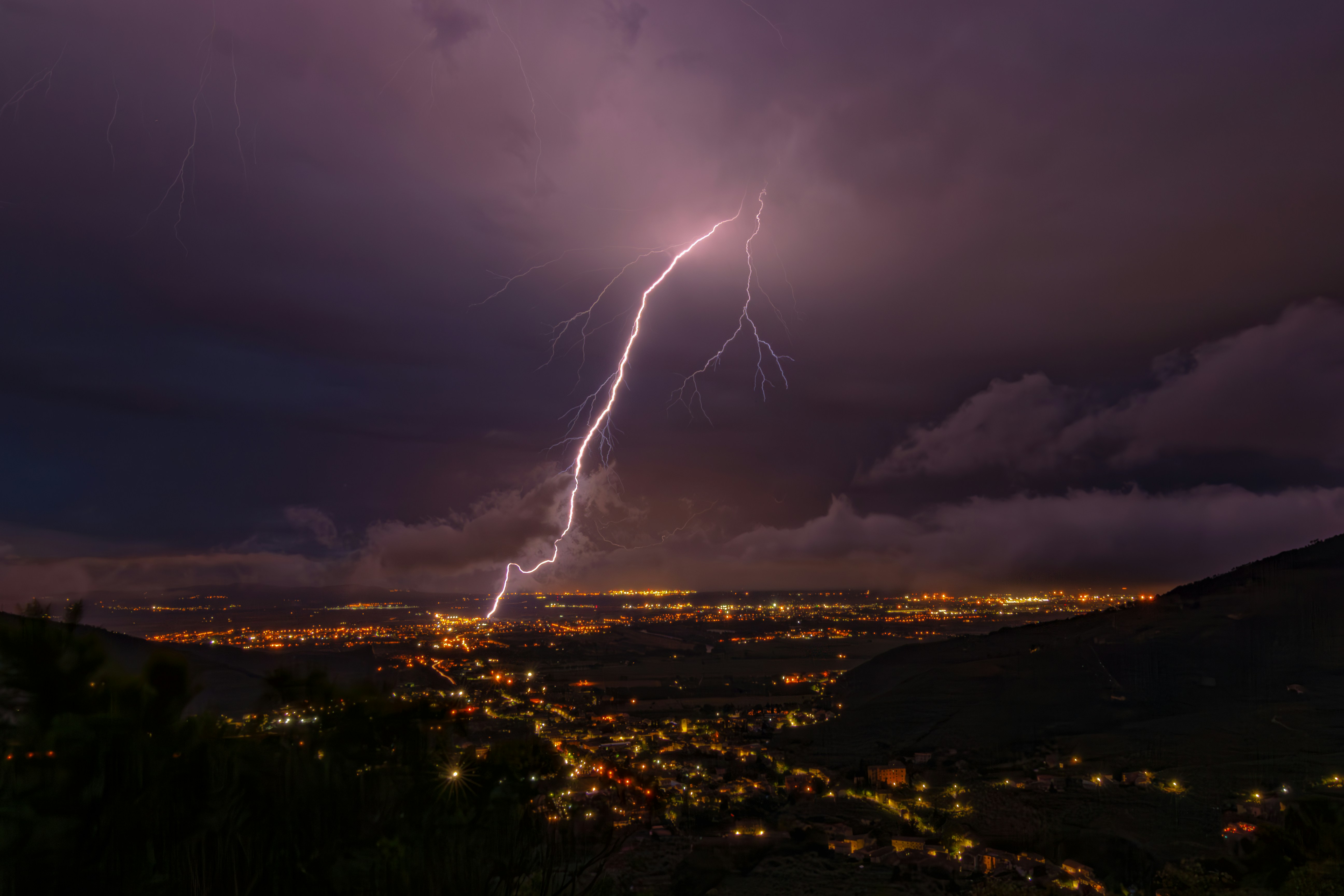 Lightning strikes illuminate a city at night.